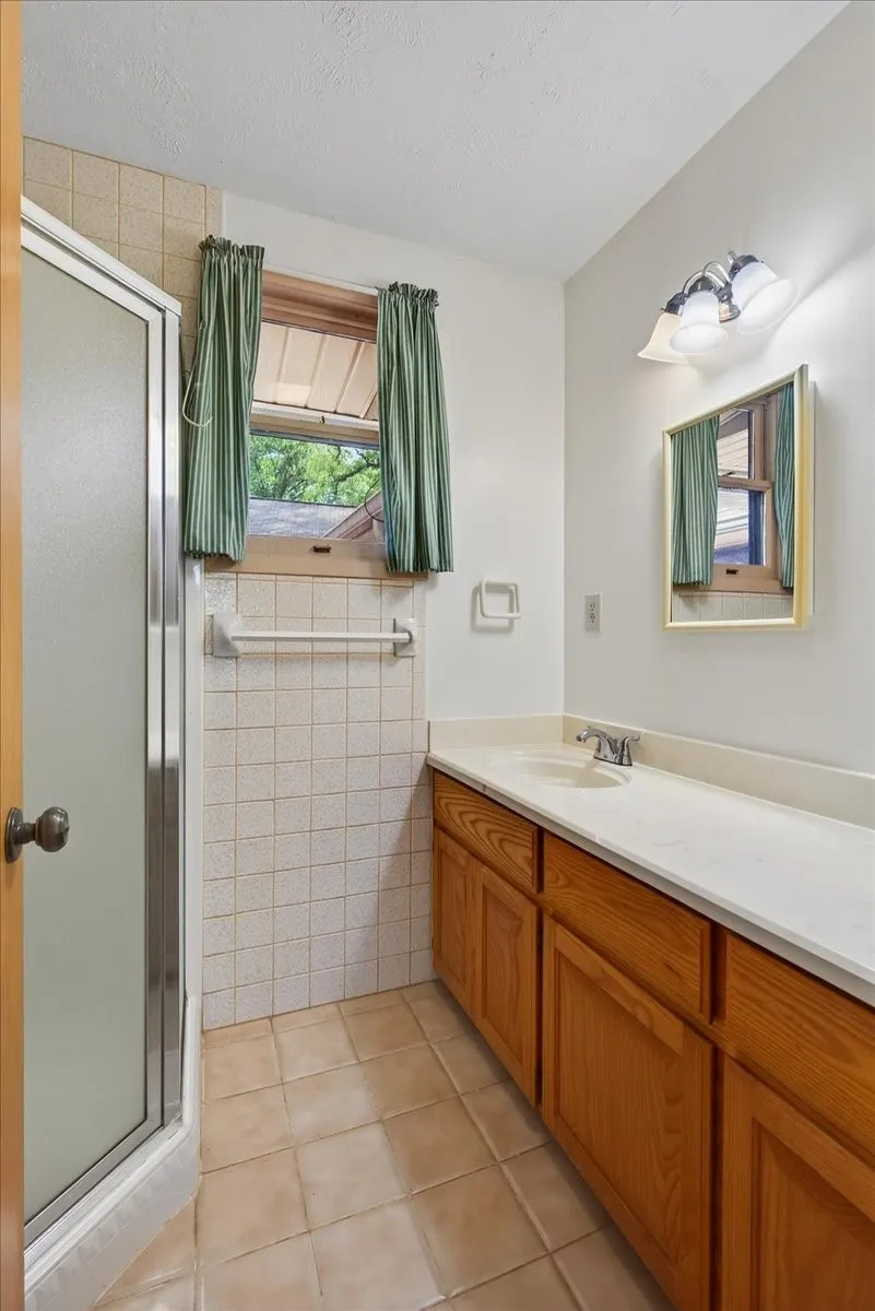 Bathroom with vanity, a shower stall, light tile patterned floors, and tile walls