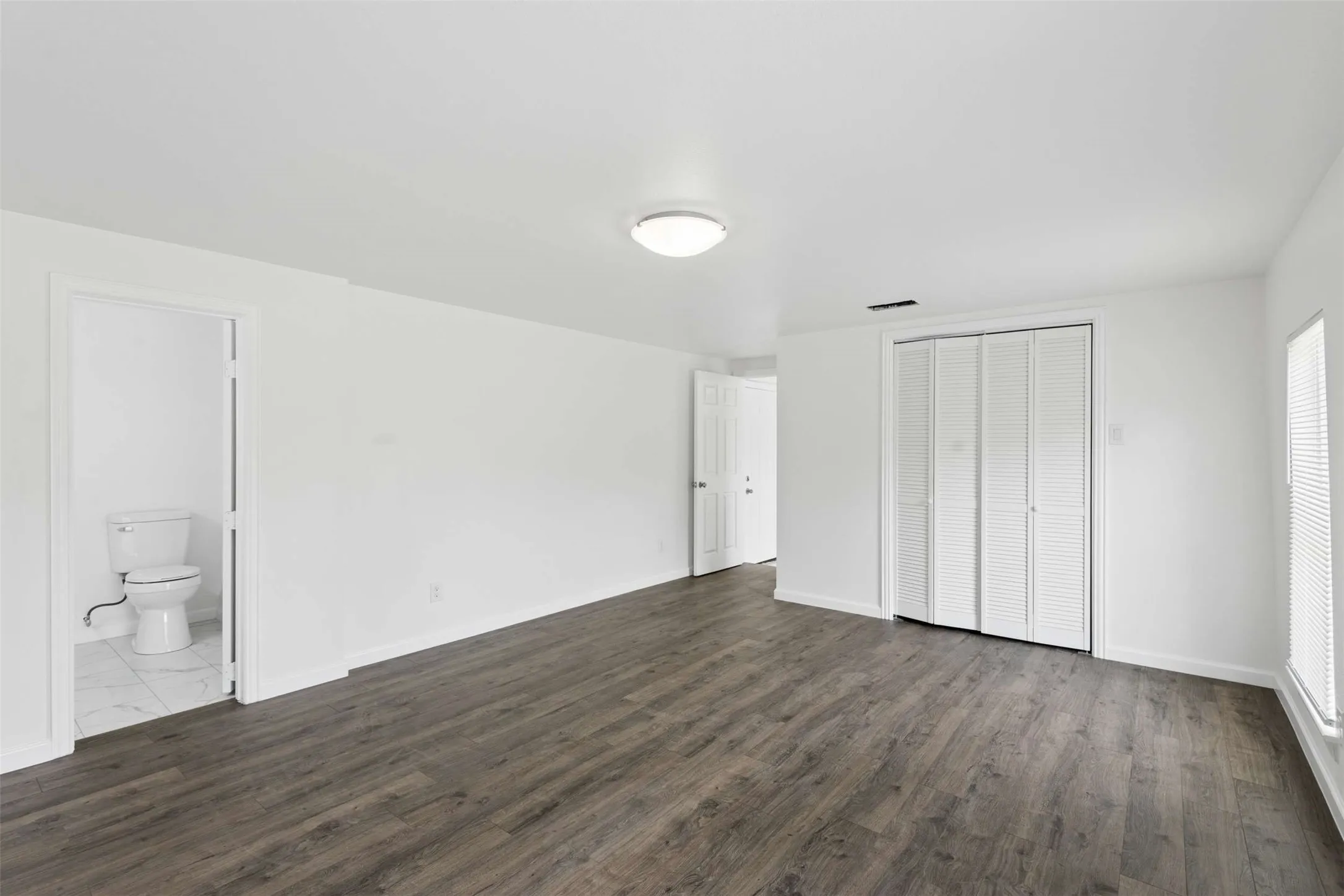 Unfurnished bedroom featuring a closet, dark wood finished floors, and ensuite bathroom