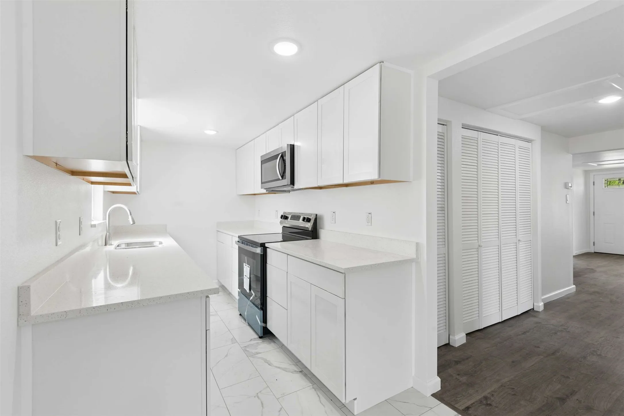 Kitchen with stainless steel appliances, white cabinetry, light stone countertops, light marble finish flooring, and recessed lighting