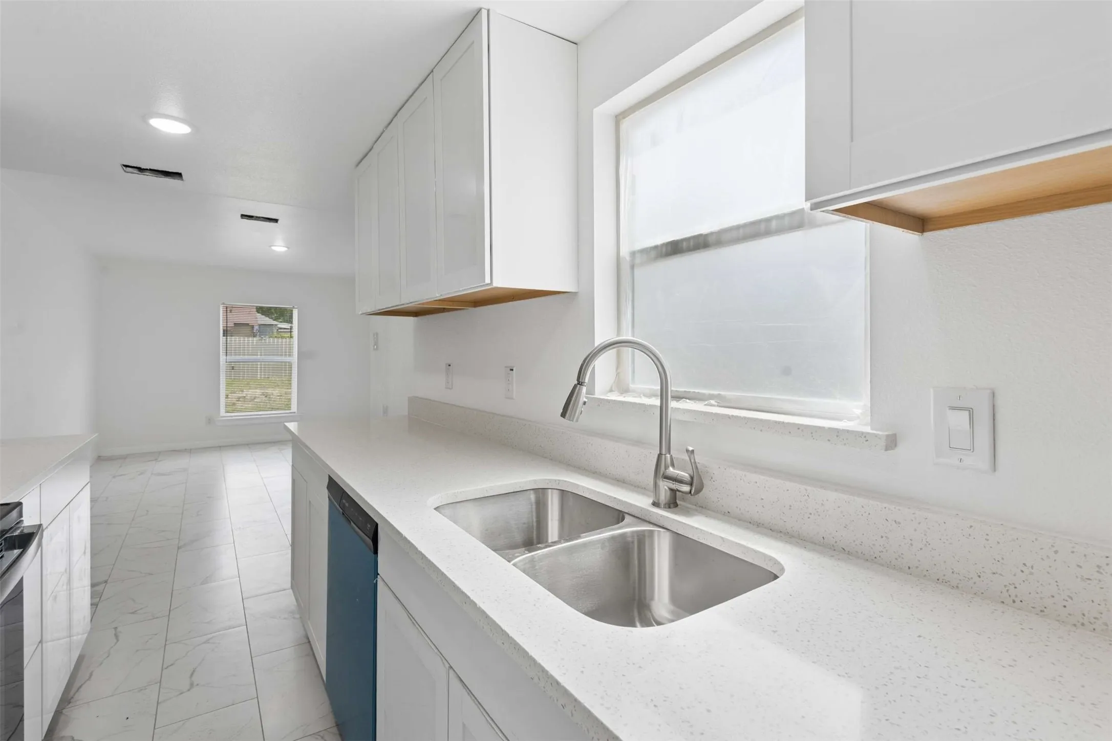 Kitchen with white cabinetry, dishwashing machine, light stone counters, and light marble finish floors