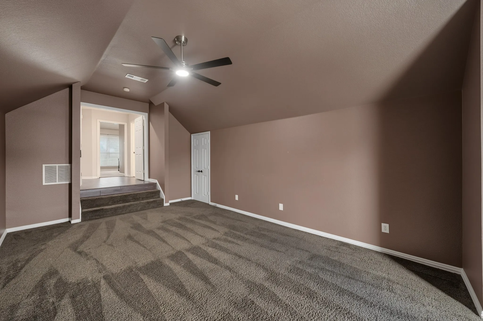 Spacious room featuring vaulted ceilings, a ceiling fan with integrated lighting, and plush patterned carpeting