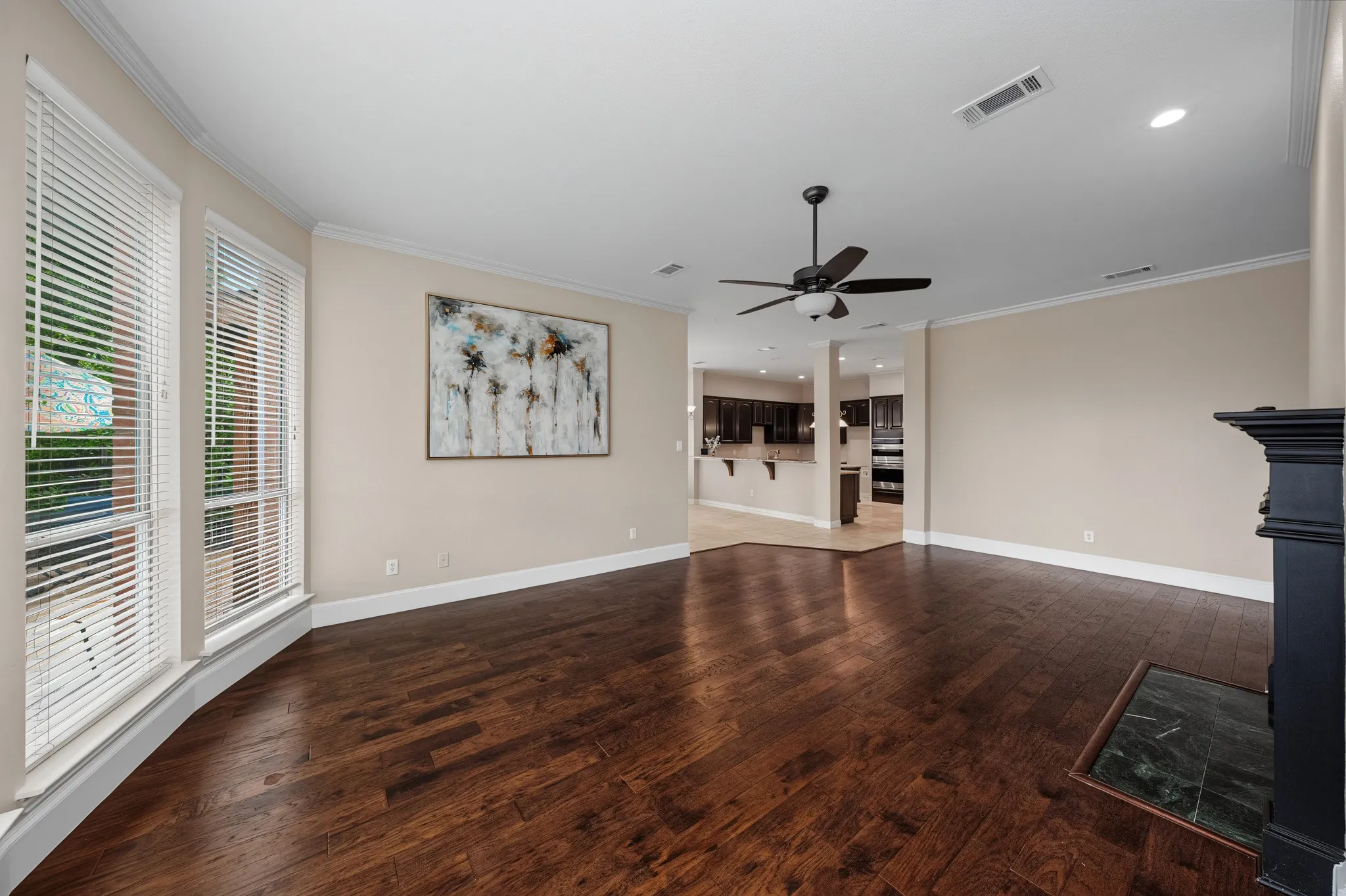 Living area featuring wood-finish flooring, a black mantle with a stone hearth, and a ceiling fan with integrated lighting