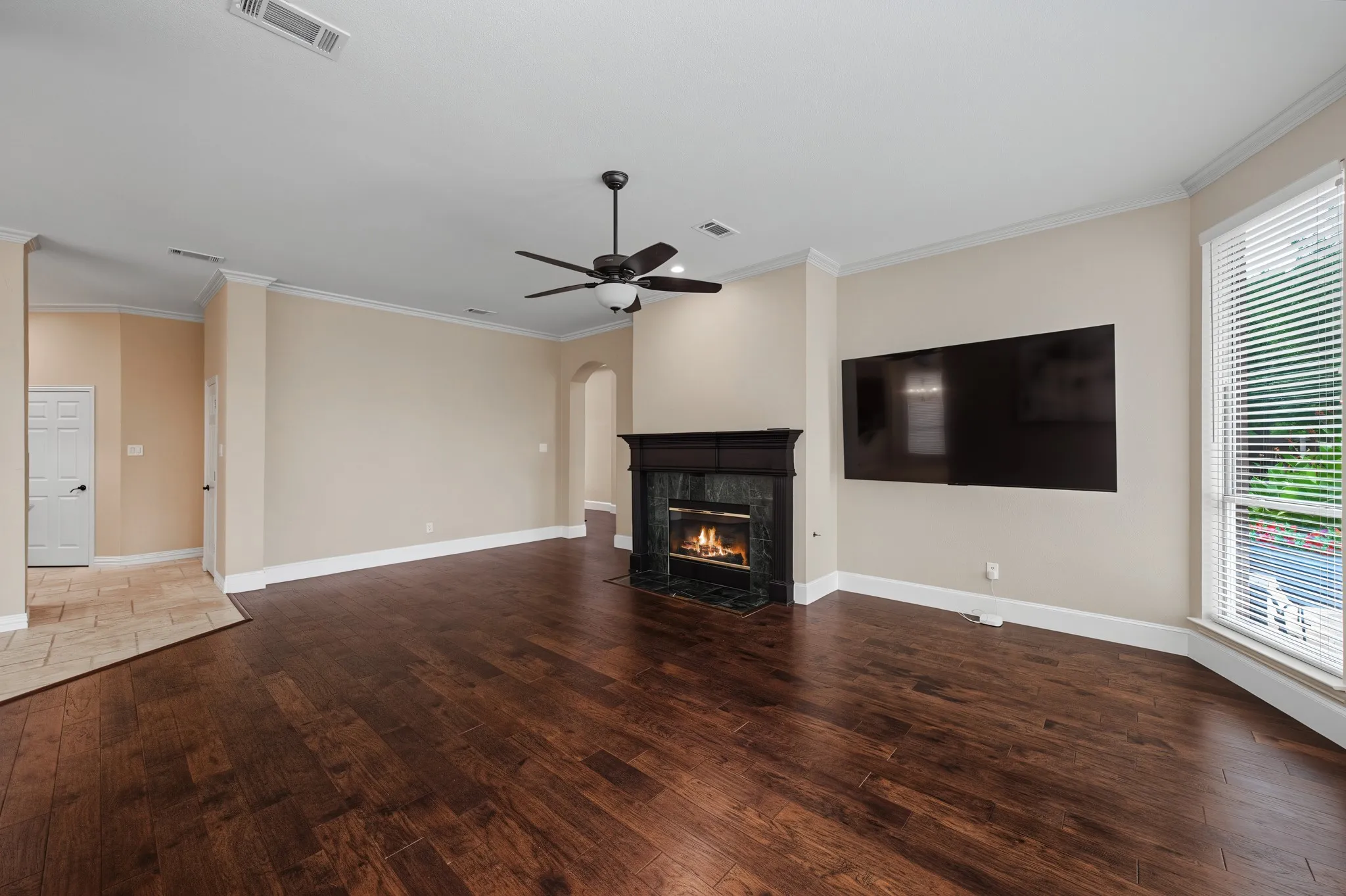 Spacious interior featuring rich wood-finish flooring, a fireplace with a dark stone surround and mantel, and crown molding