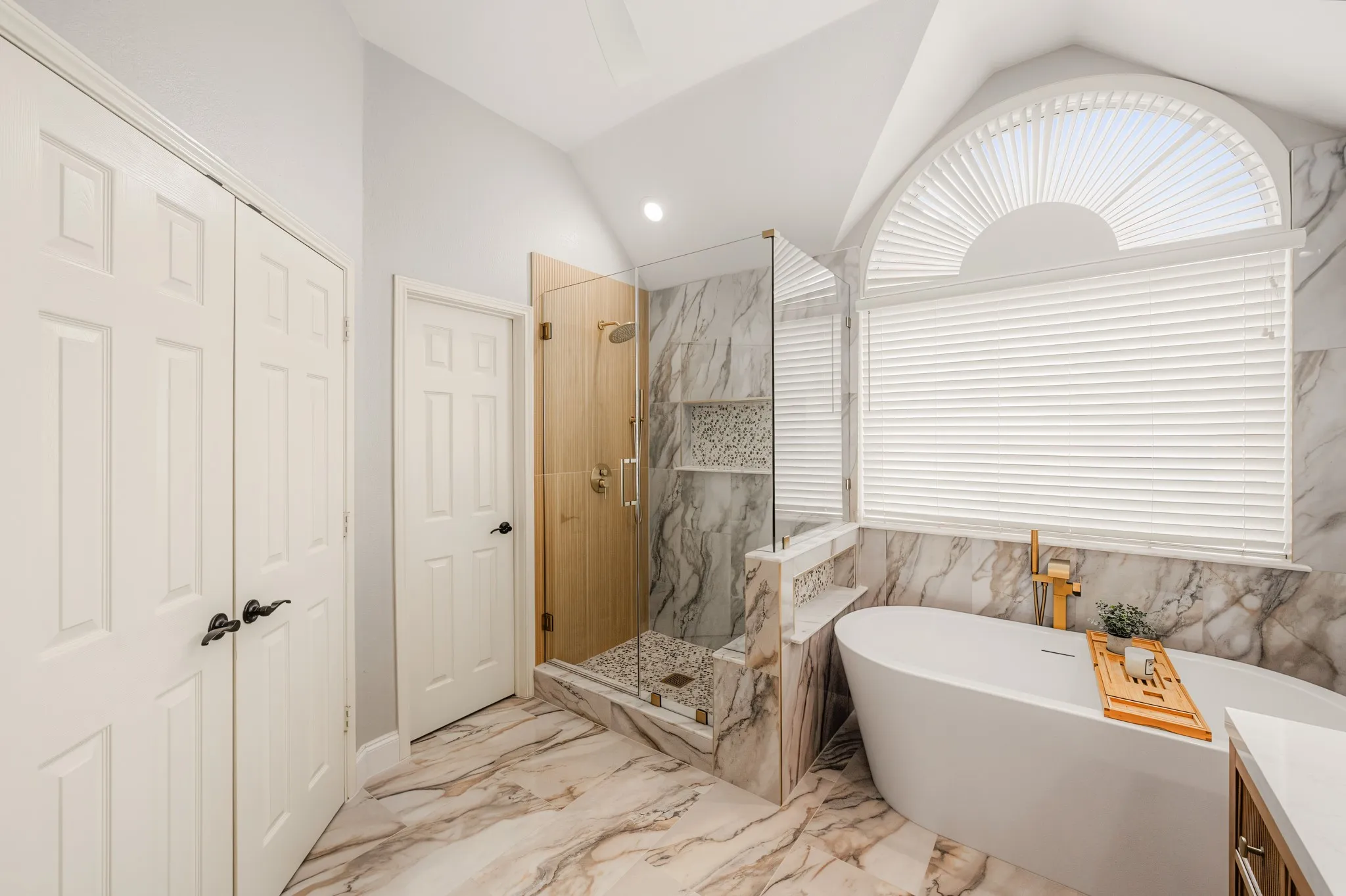 Freestanding soaking tub with gold-tone fixtures, complemented by a walk-in shower with glass enclosure and mosaic tile accents