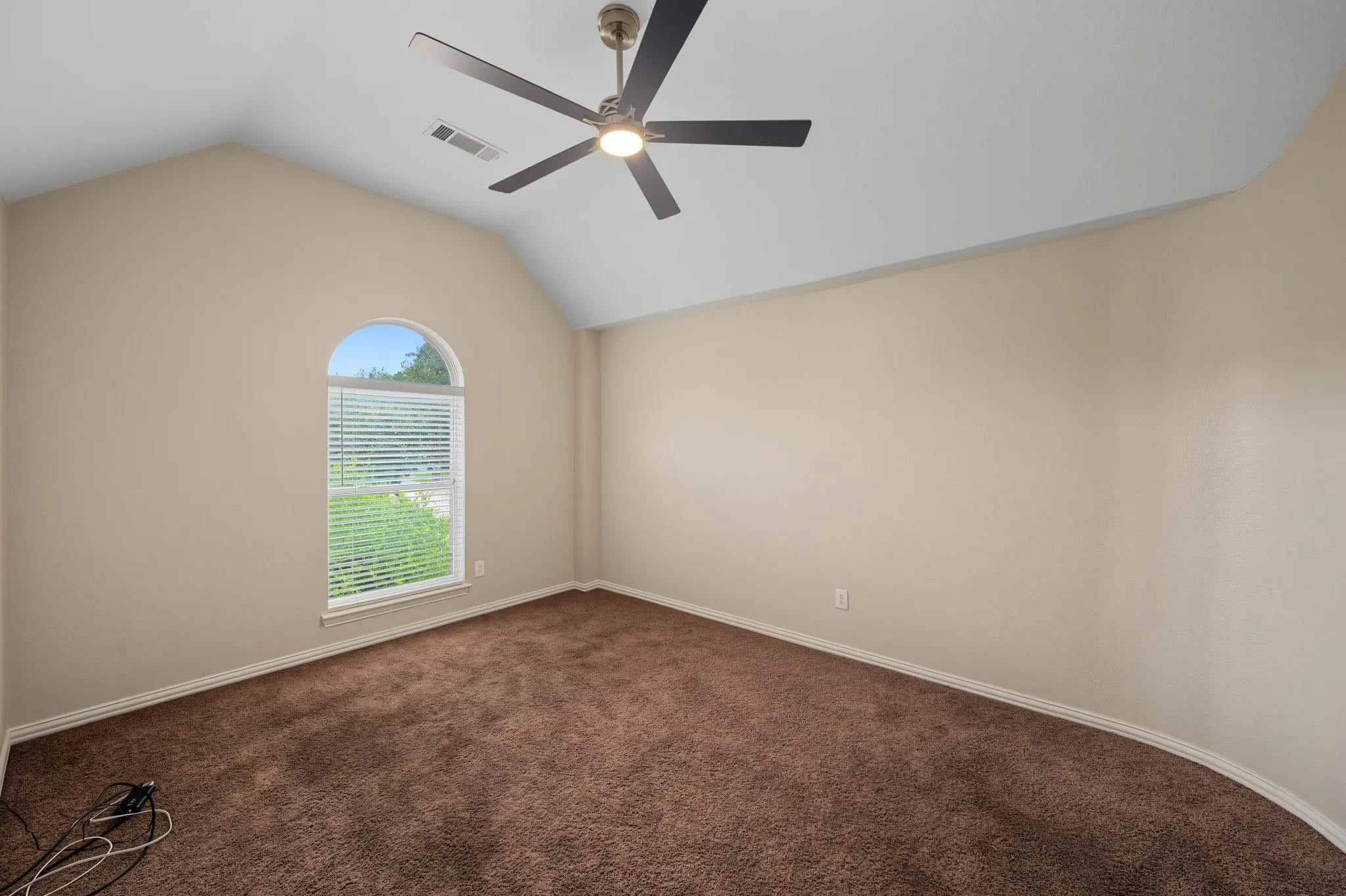Vaulted ceiling room featuring a large arched window with blinds, a ceiling fan with integrated lighting, and neutral wall paint