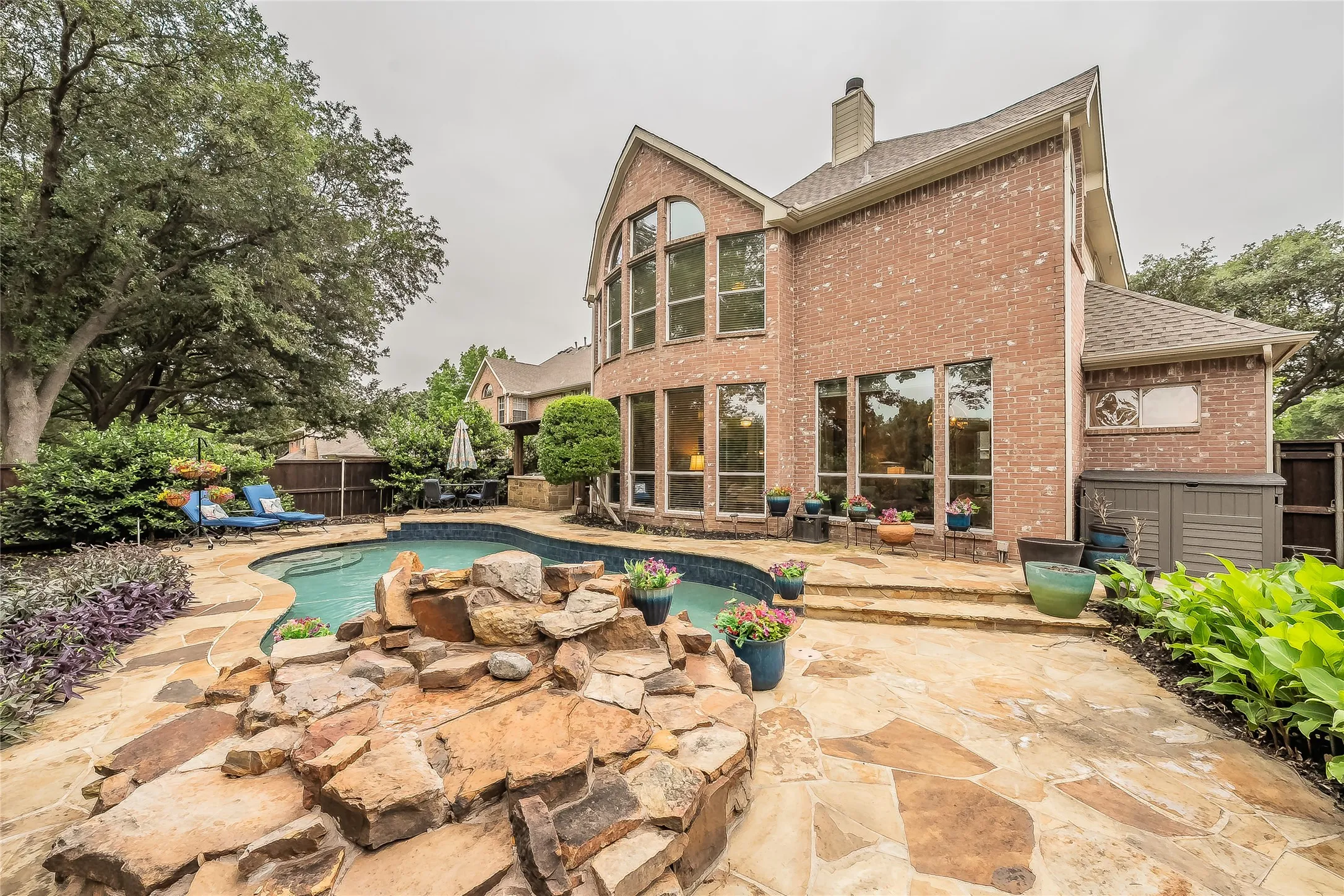 Brick exterior featuring a multi-level roofline, an arched window, and a wall of windows overlooking a freeform pool