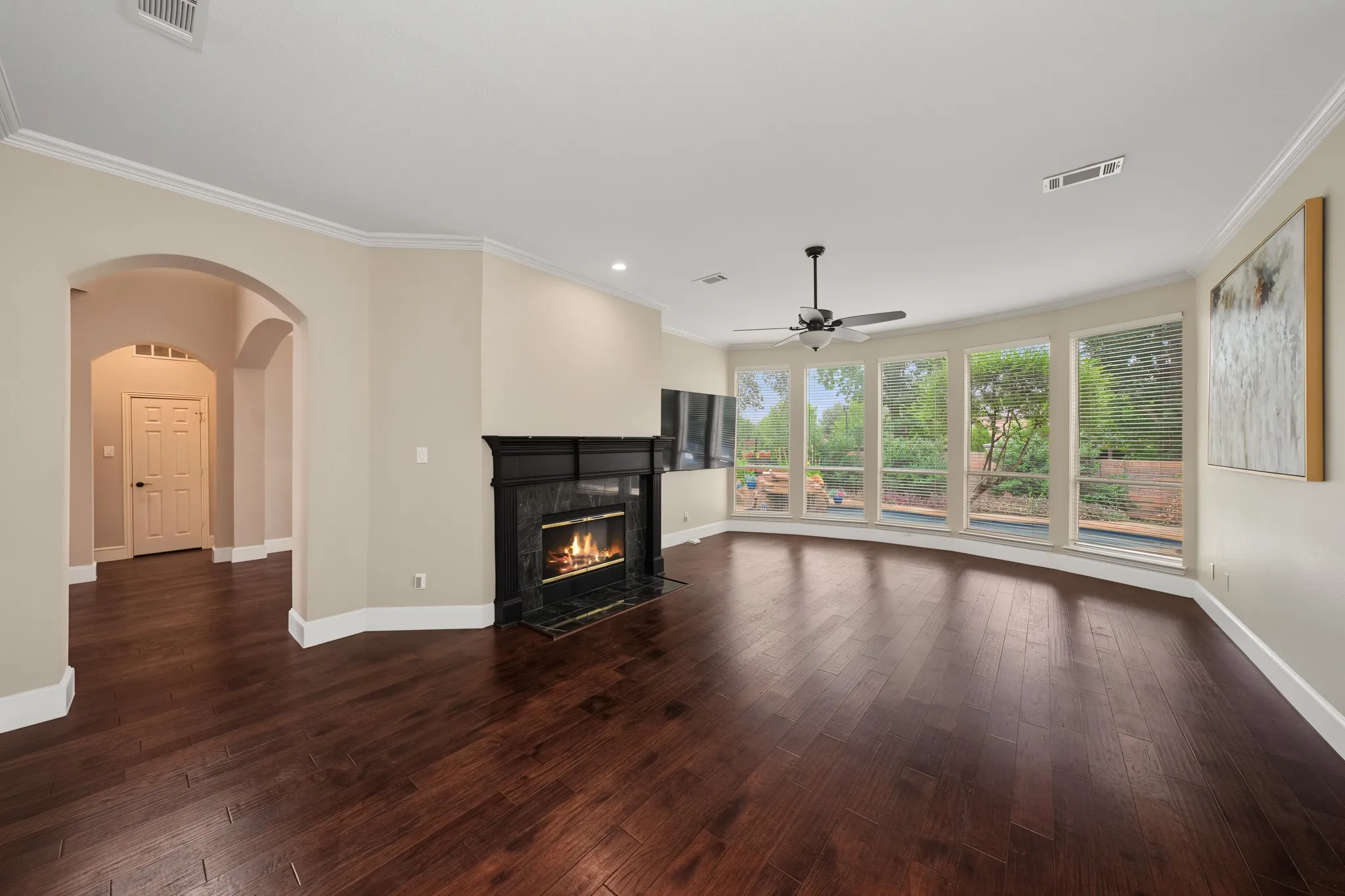 Spacious room featuring wood-finish flooring, a contemporary fireplace with a dark stone surround, and a ceiling fan