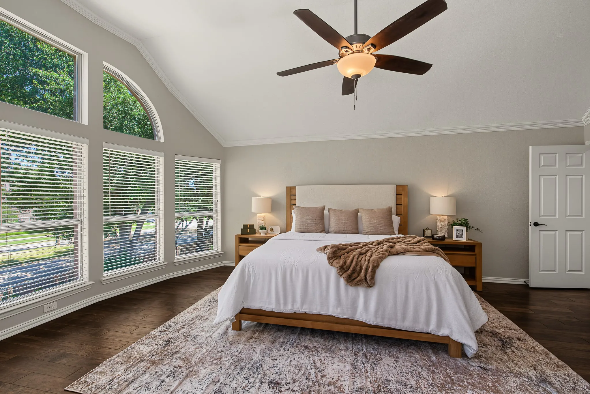 Vaulted ceiling with an attached ceiling fan, crown molding, wood-finish flooring, and multiple windows with blinds