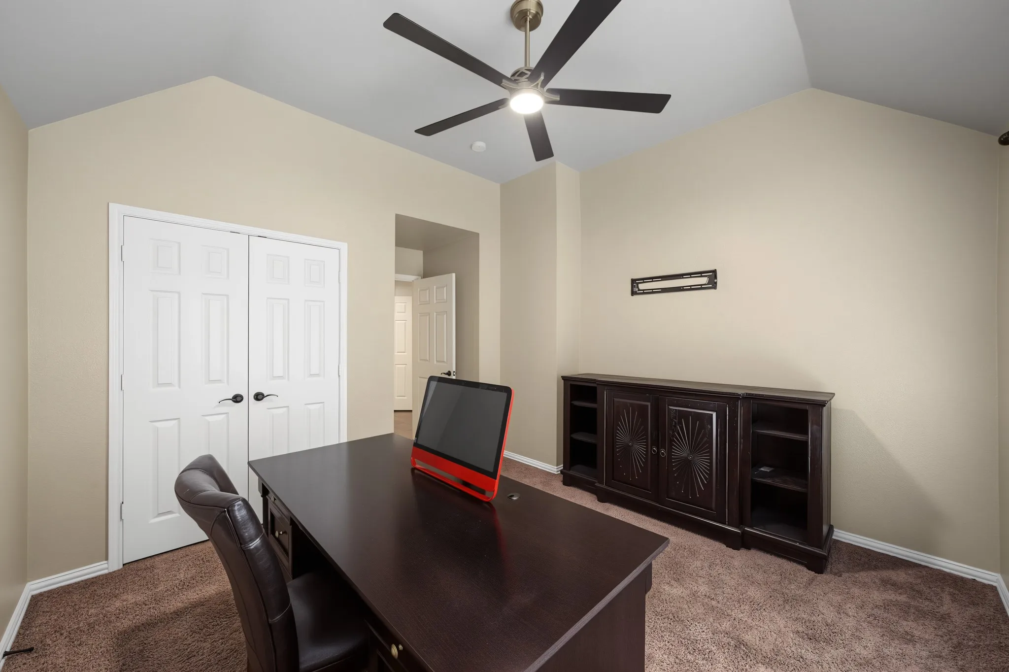 Vaulted ceiling room featuring light neutral wall paint, white paneled doors with dark hardware, and a ceiling fan with integrated lighting