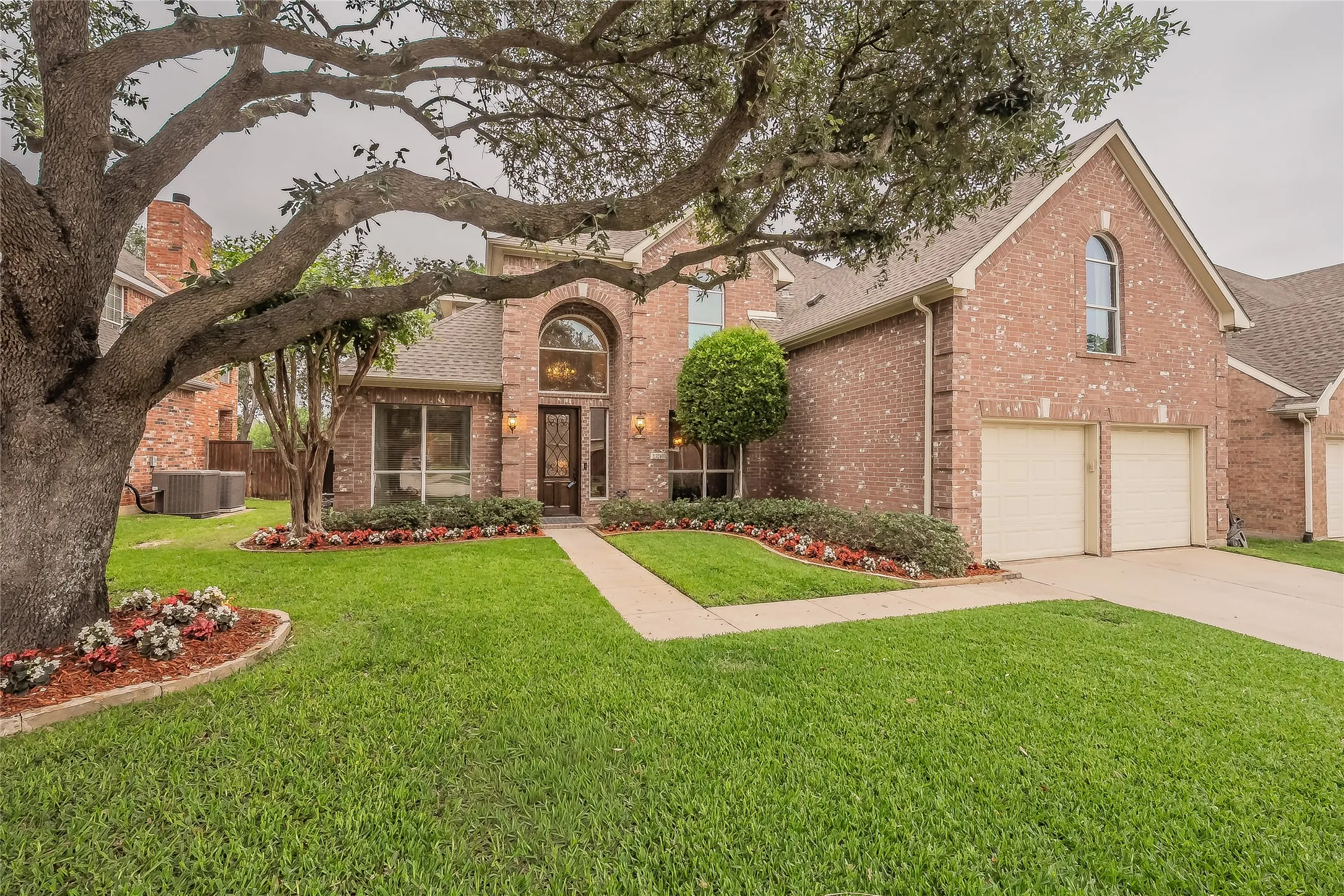 Brick exterior featuring a two-car garage, arched entry, and extensive landscaping