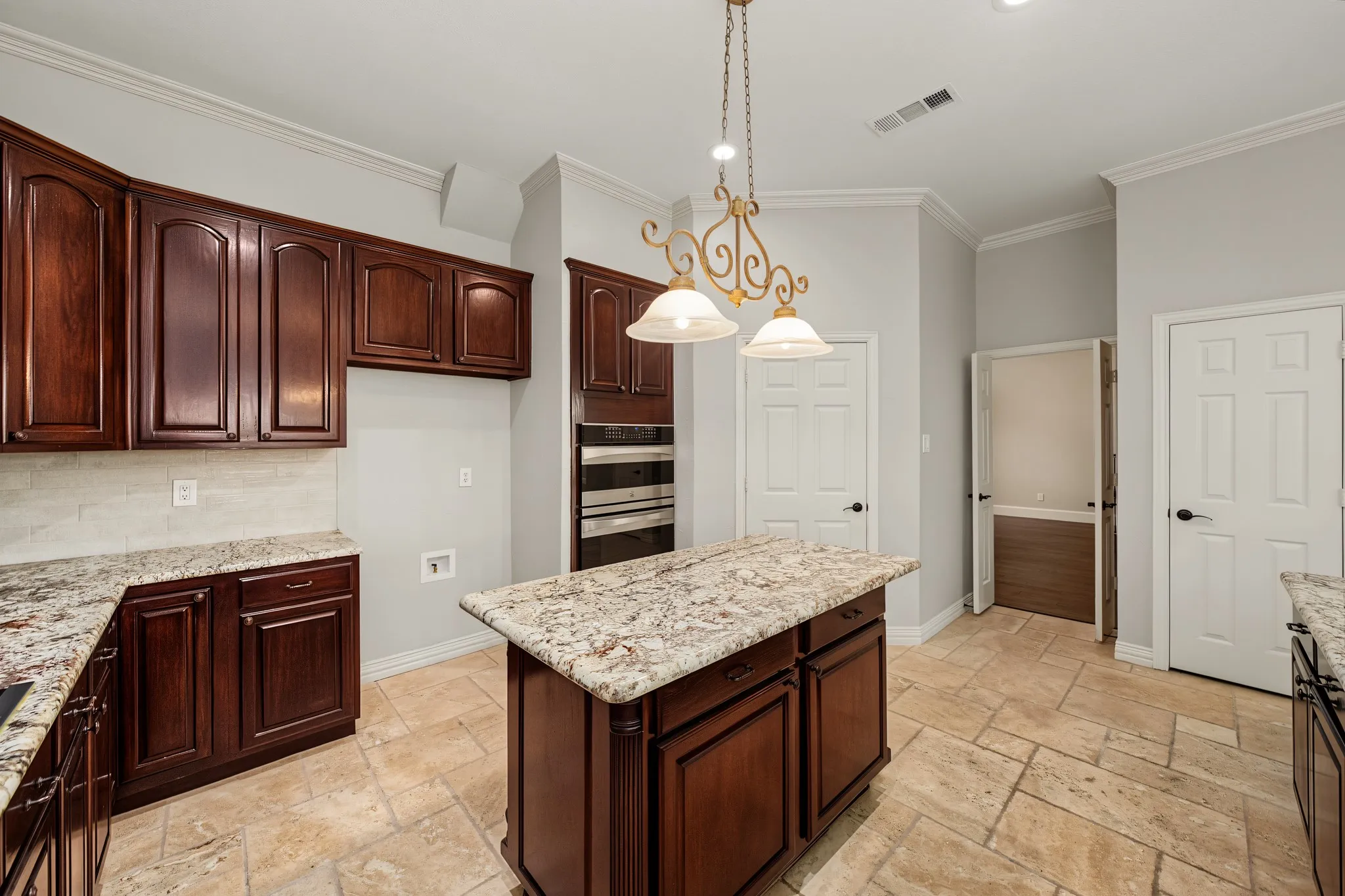 Kitchen featuring a central island with granite countertop, dark wood cabinetry, built-in double ovens, and tile flooring