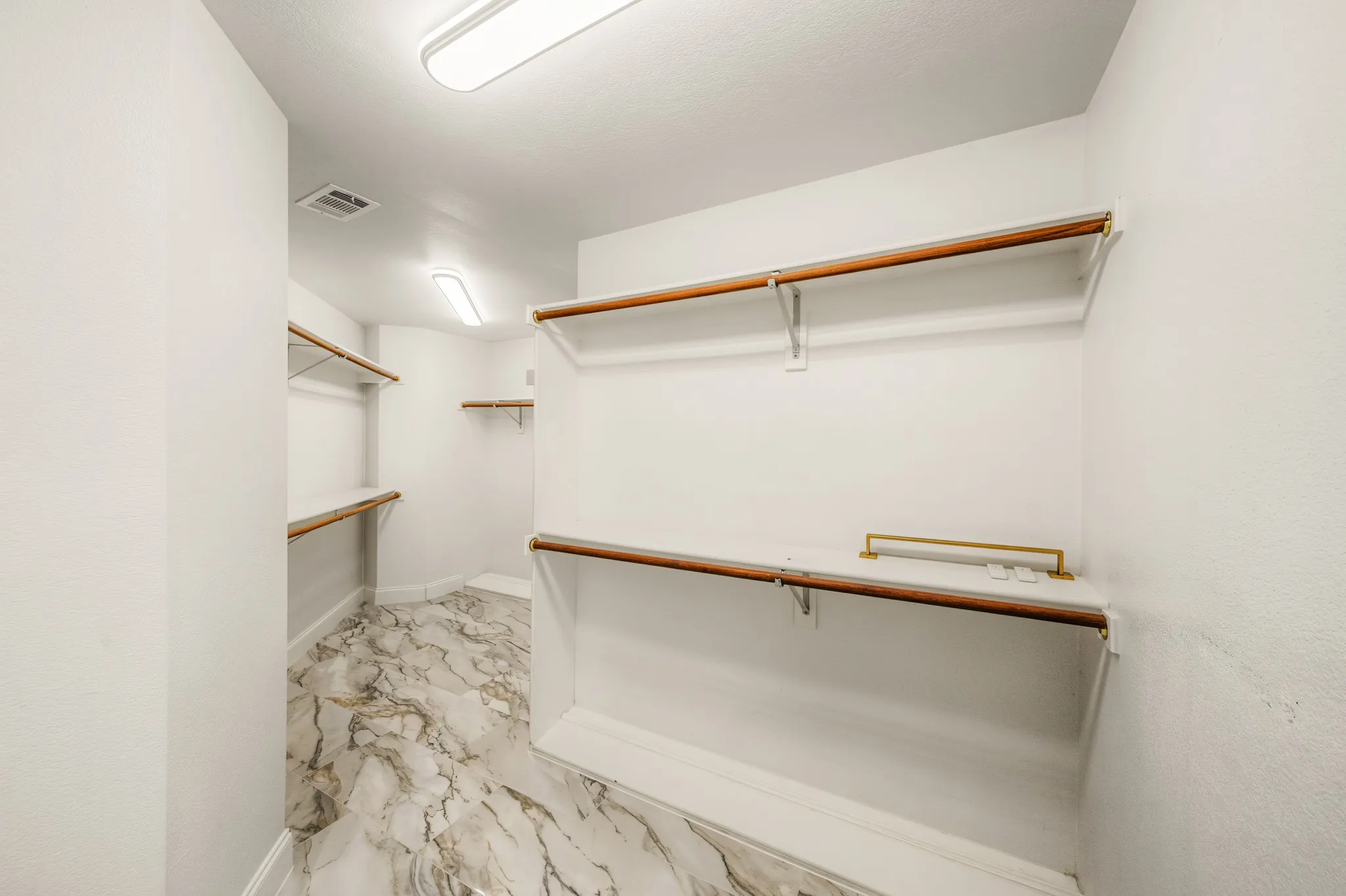 Spacious closet featuring marble-look flooring, multiple wood-finish hanging rods, white shelving, and recessed lighting