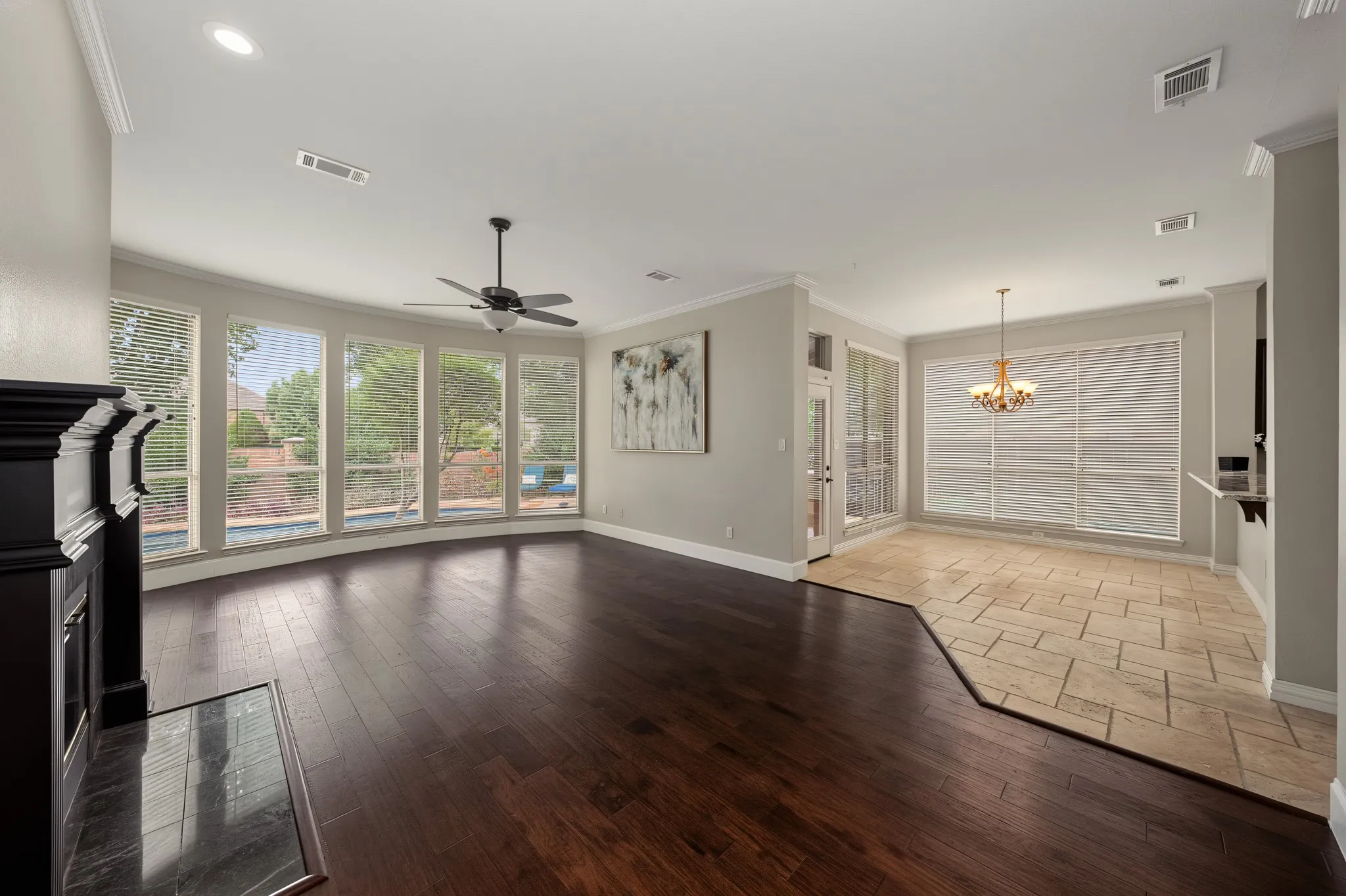 Spacious living area featuring wood-finish flooring, a fireplace with a dark mantel, and a wall of windows overlooking the outdoor pool