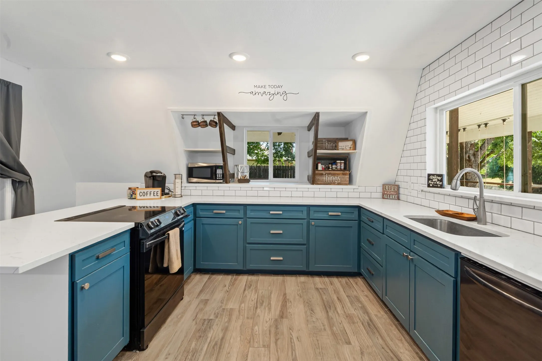 Kitchen with blue cabinets, black range with electric stovetop, light stone counters, dishwashing machine, and a peninsula