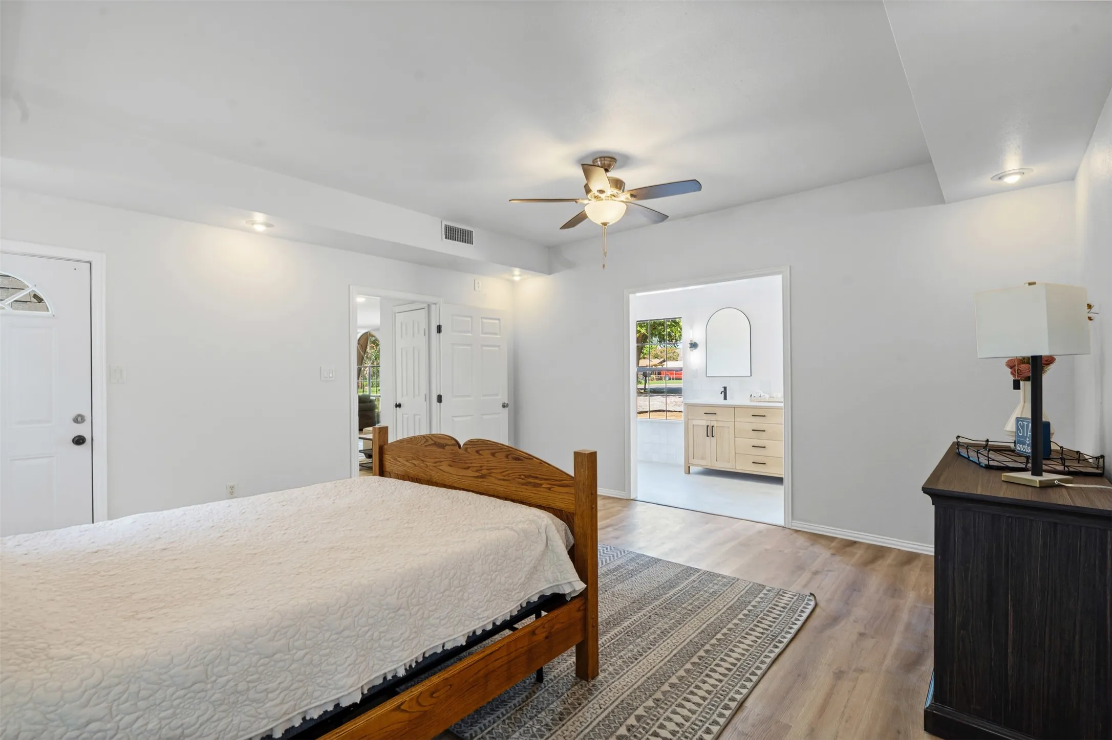 Bedroom with light wood-style flooring, ceiling fan, and ensuite bath
