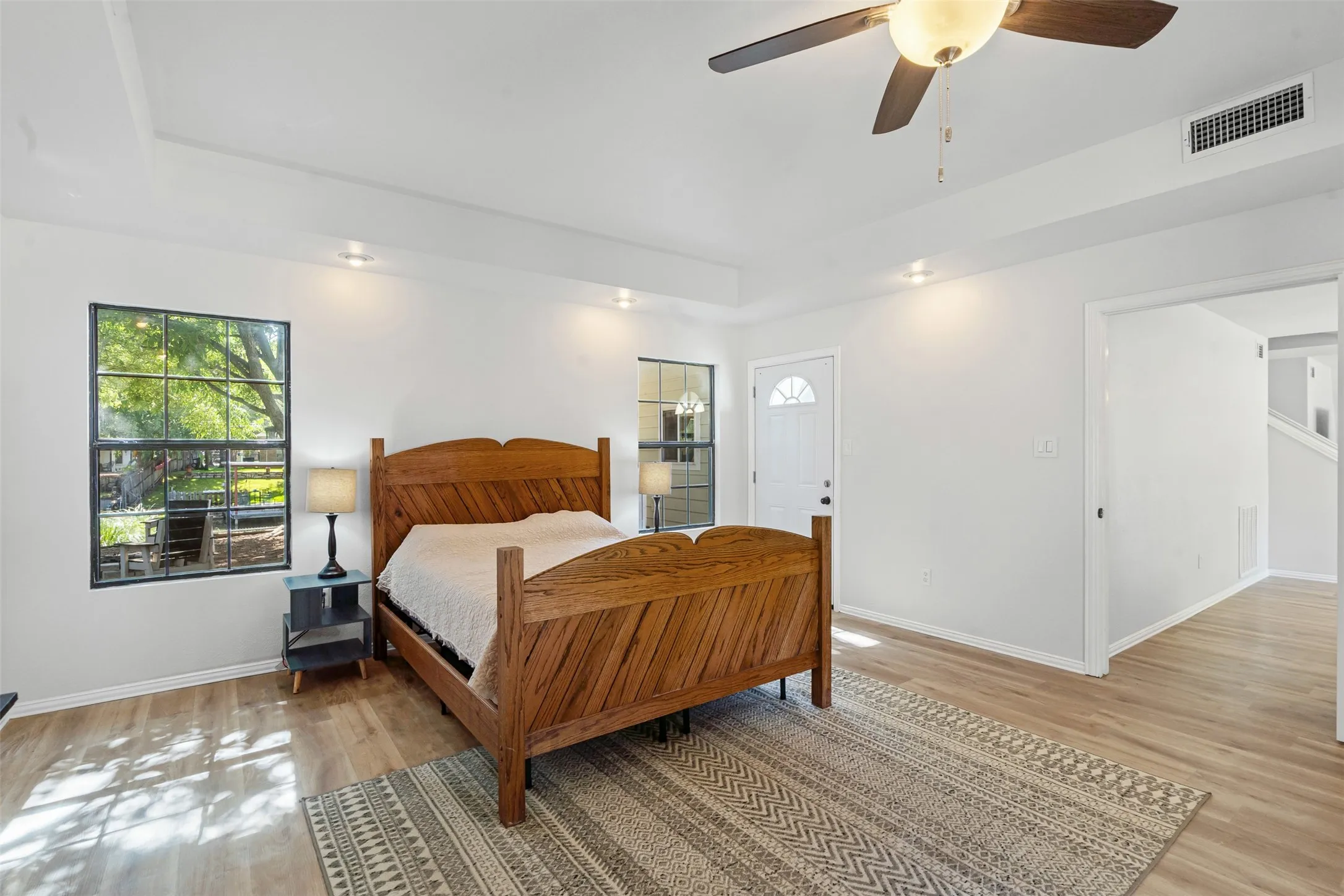Bedroom featuring a raised ceiling, light wood-style flooring, and ceiling fan