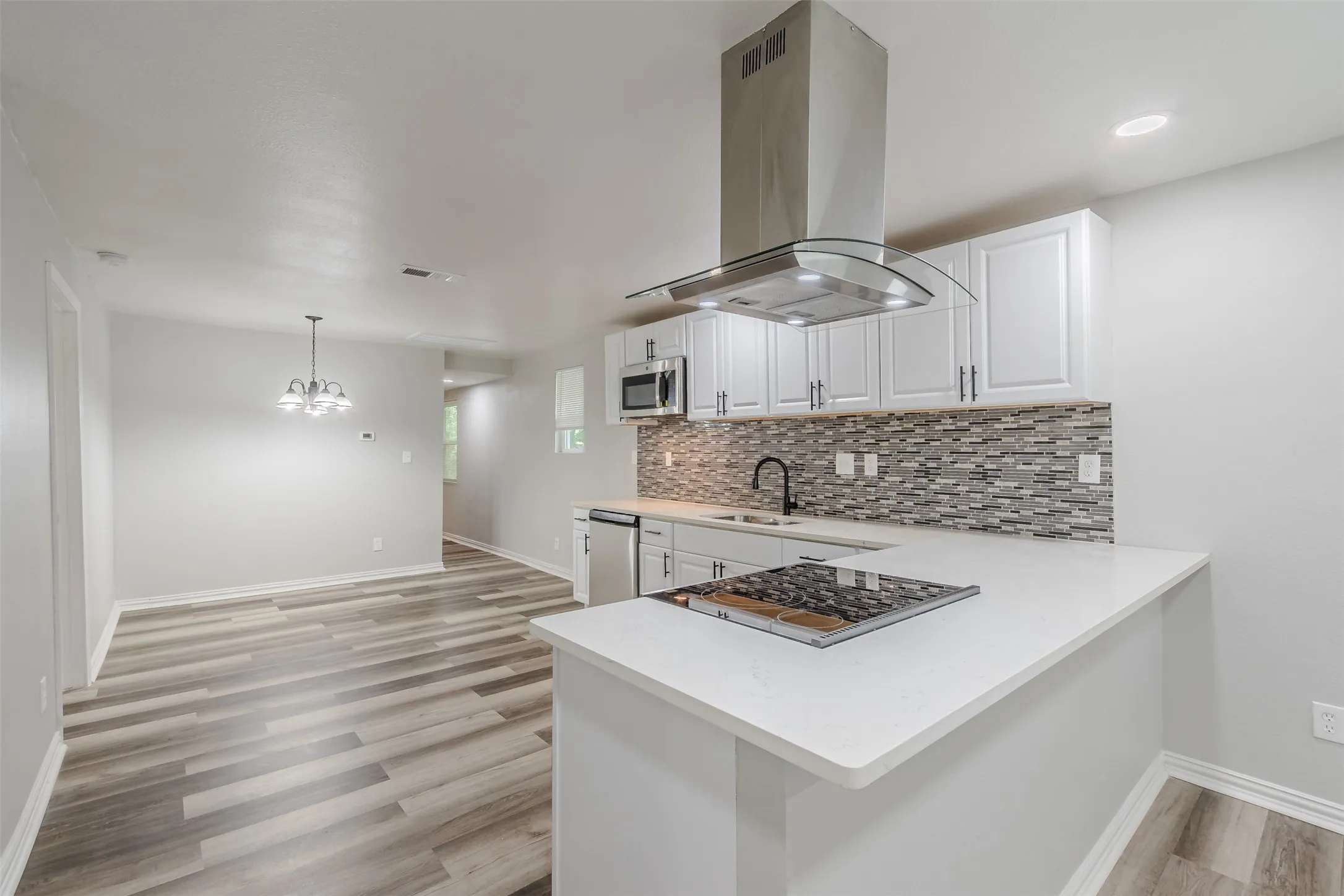 Kitchen with island range hood, white cabinets, a peninsula, and light wood-type flooring