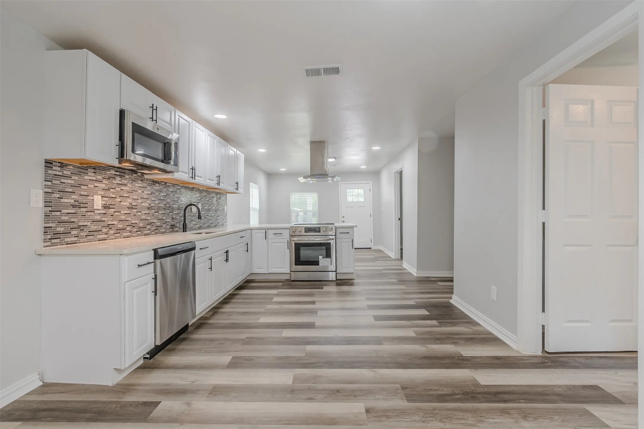 Kitchen featuring white cabinets, light countertops, stainless steel appliances, island range hood, and recessed lighting