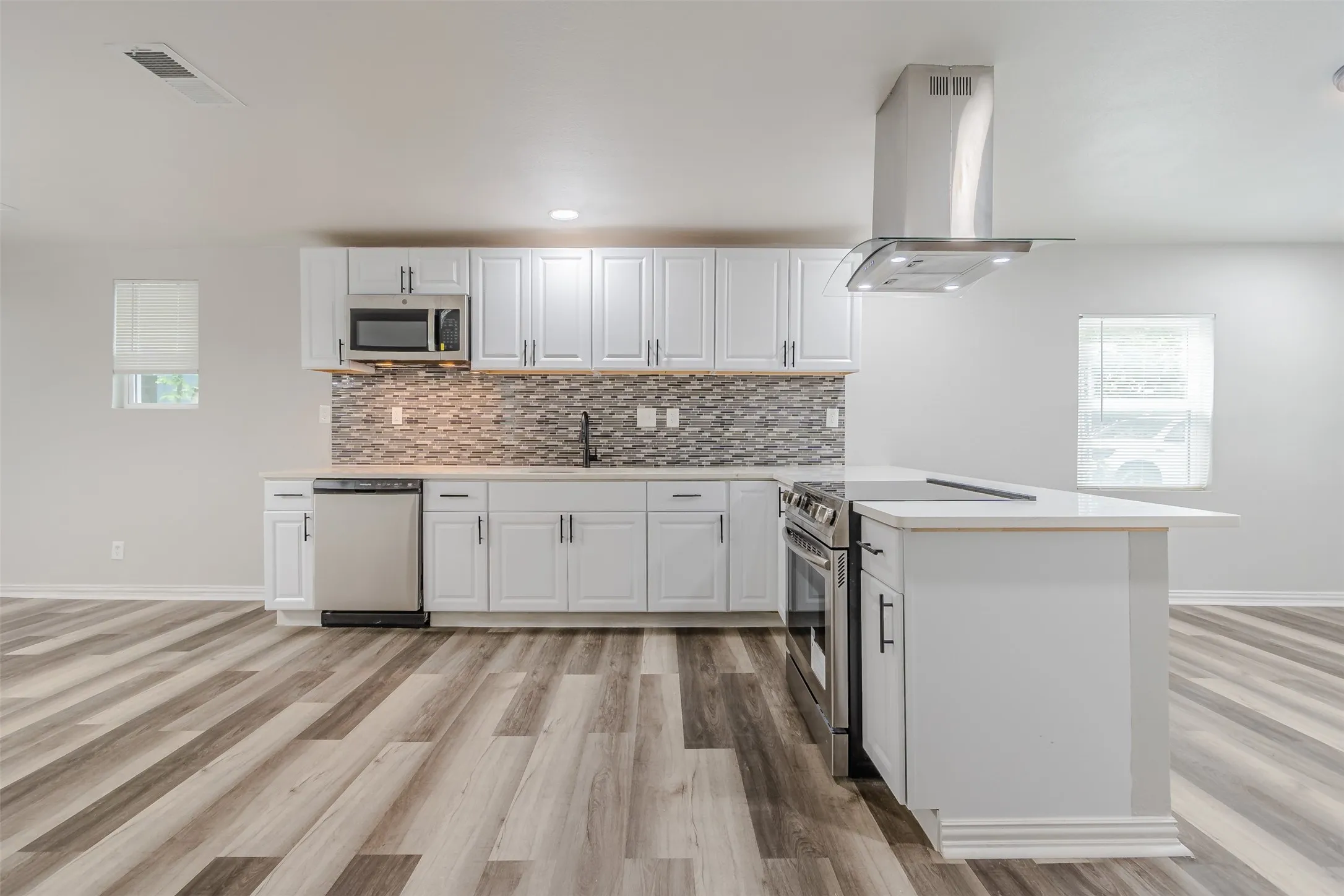 Kitchen featuring island exhaust hood, stainless steel appliances, white cabinetry, light wood-style flooring, and a peninsula