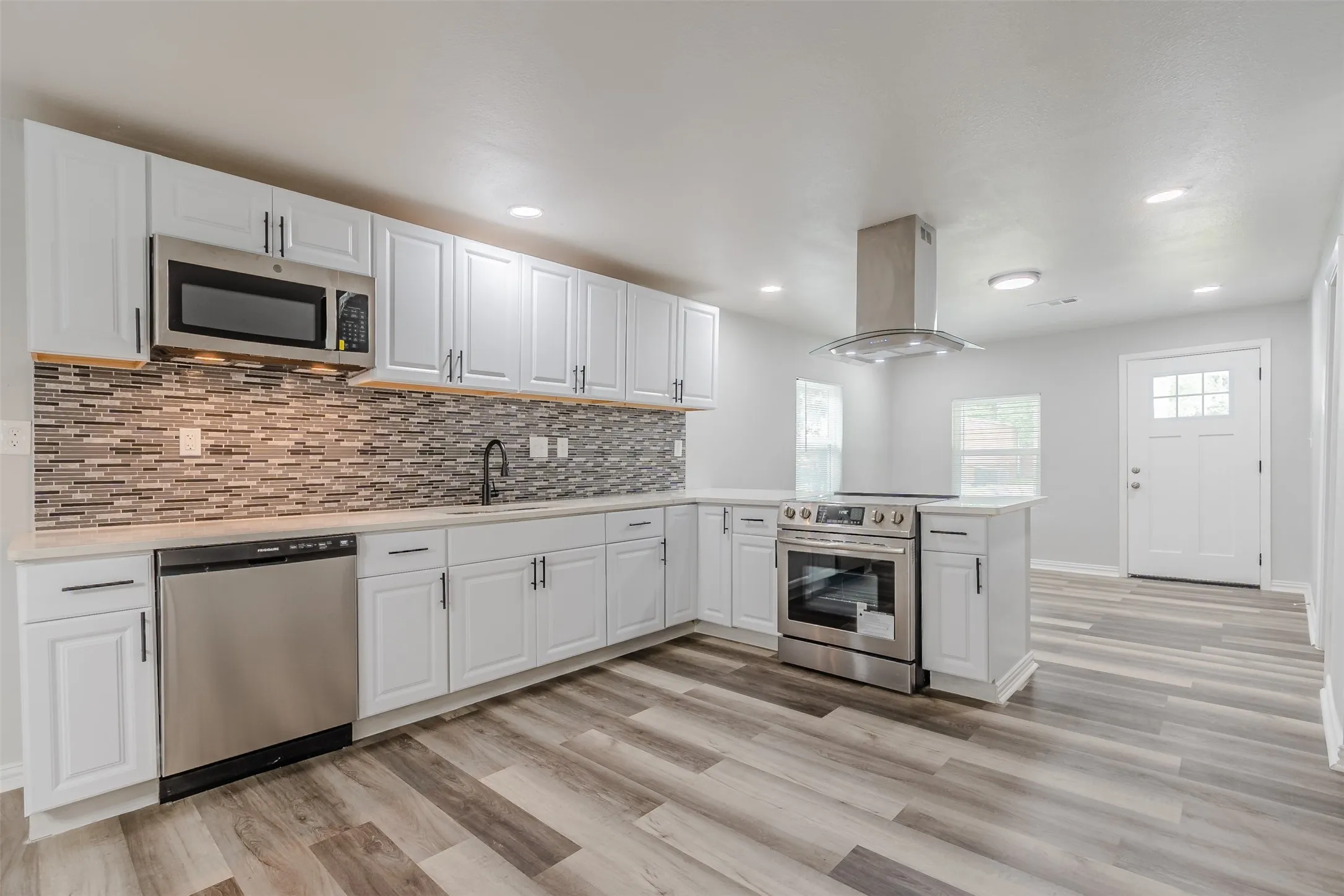 Kitchen with a peninsula, white cabinetry, stainless steel appliances, island range hood, and recessed lighting