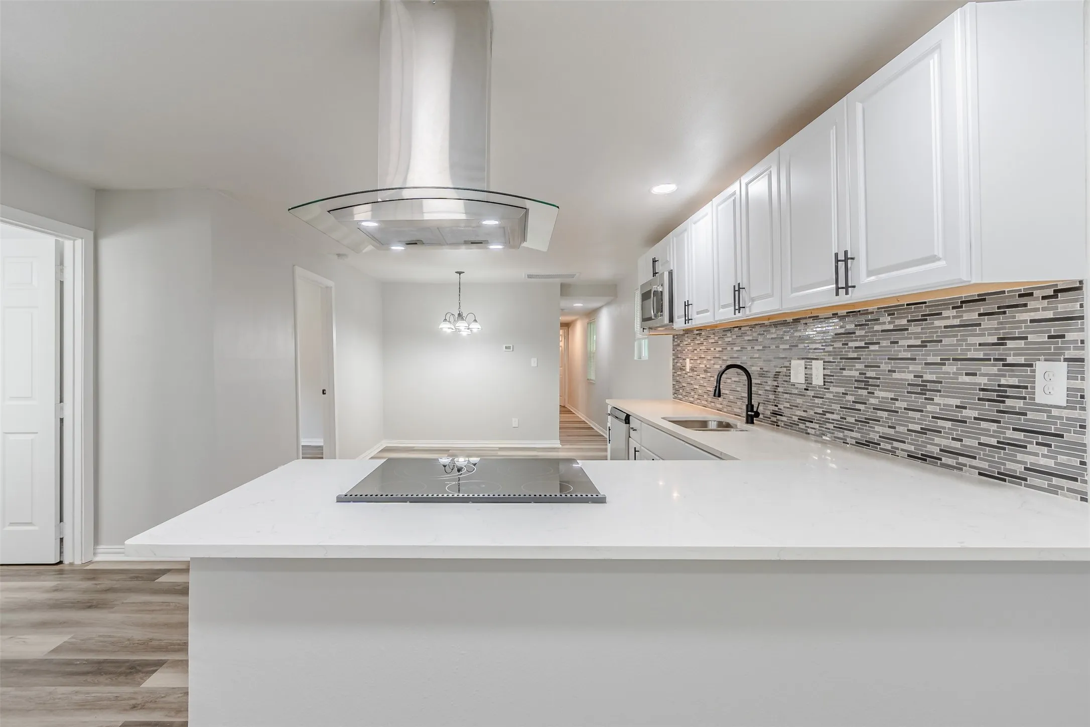 Kitchen with island exhaust hood, white cabinets, light stone counters, light wood finished floors, and a peninsula