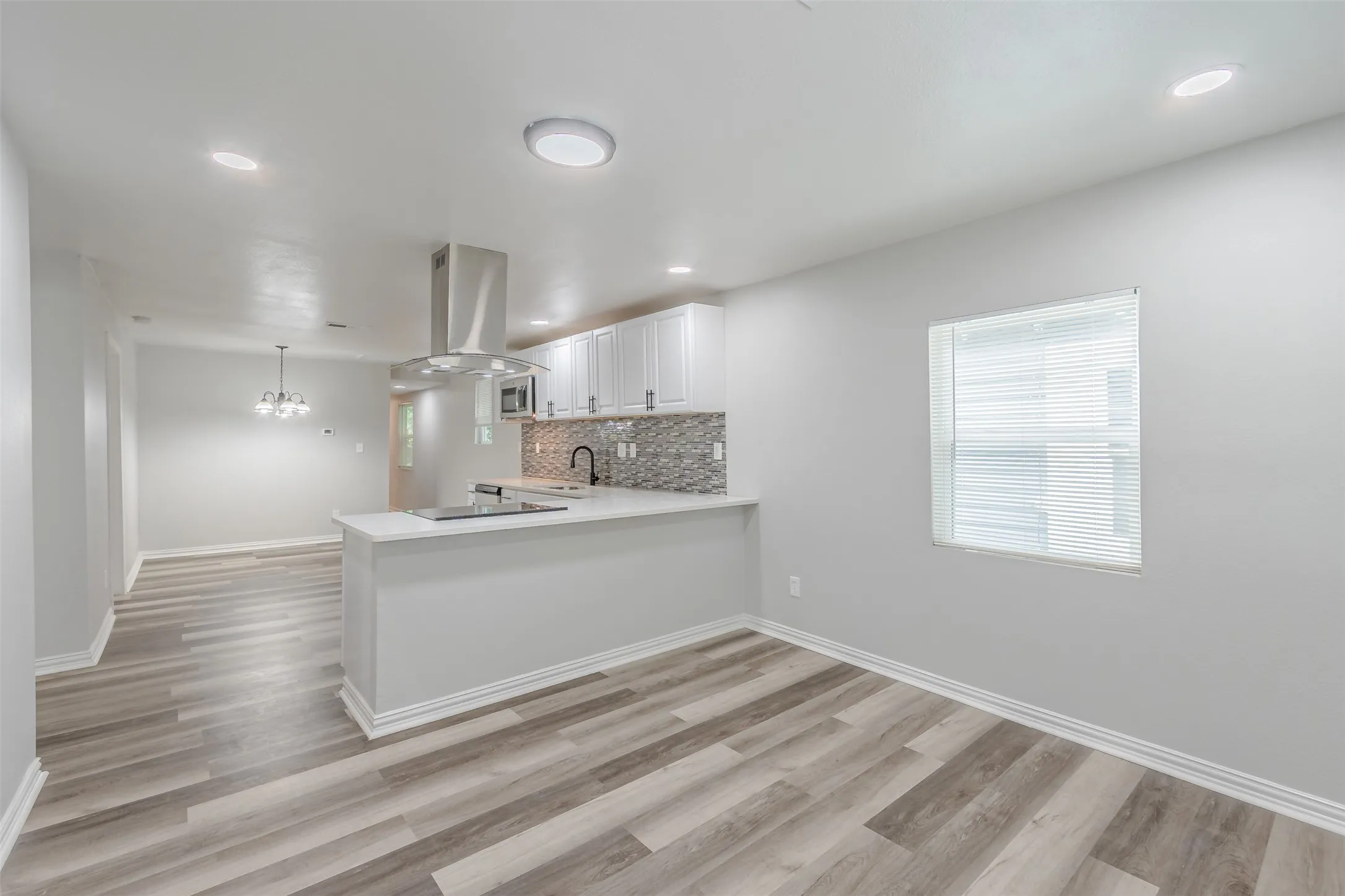 Kitchen with a peninsula, white cabinets, tasteful backsplash, light wood-style floors, and island range hood