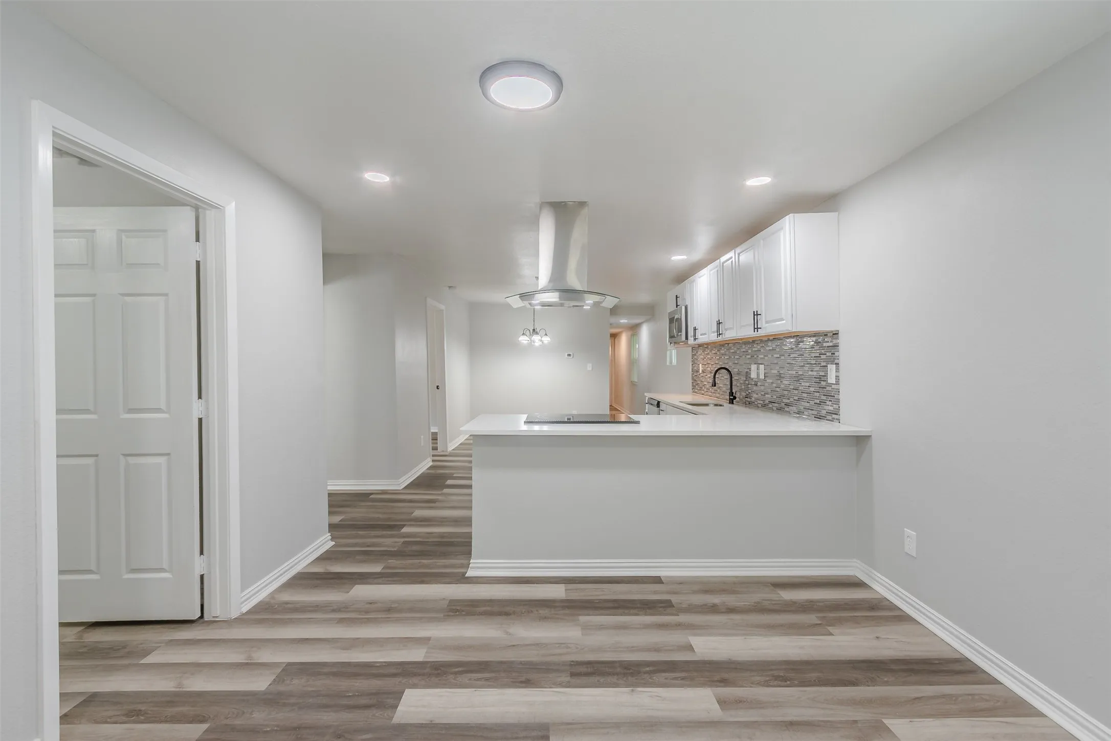 Kitchen with a peninsula, light wood-style flooring, extractor fan, white cabinets, and decorative backsplash