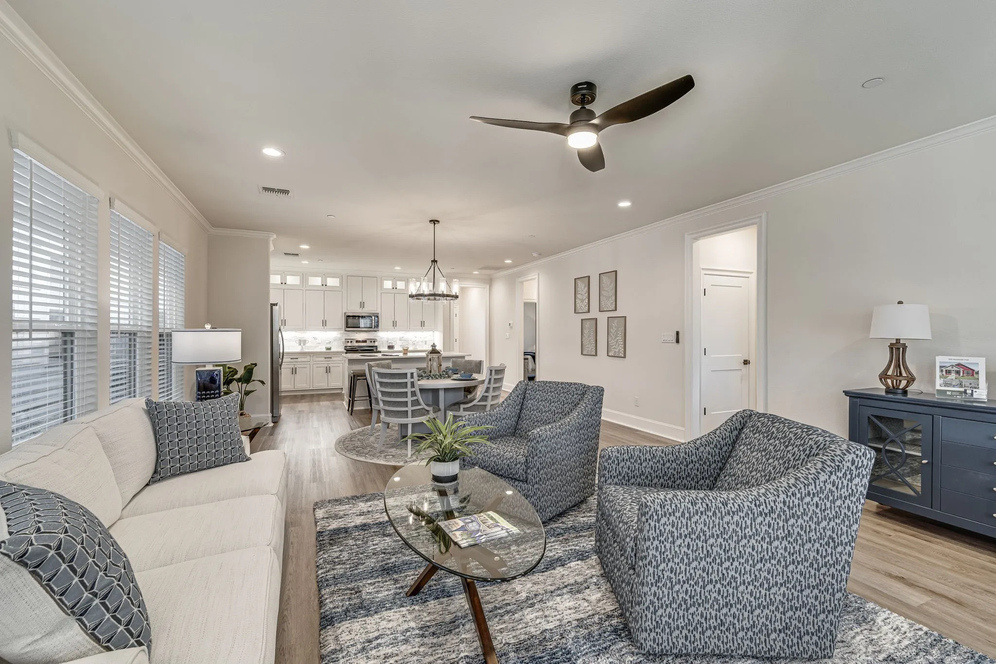 Living room with ceiling fan, suspended lighting, ornamental molding, and light wood-style flooring