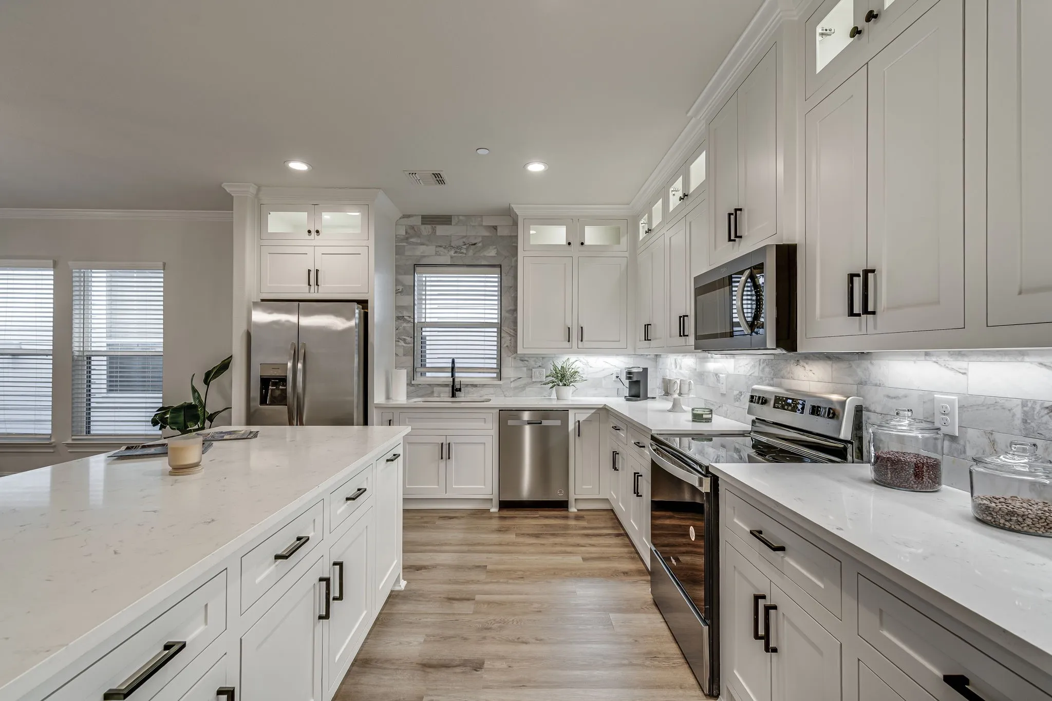 Kitchen featuring stainless steel appliances, white cabinetry, glass insert cabinets, light stone countertops, and crown molding