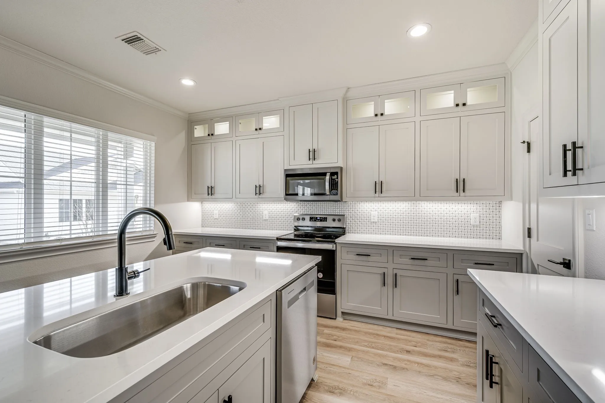 Kitchen featuring stainless steel appliances, glass fronted cabinets, backsplash, light wood-style flooring, and ornamental molding
