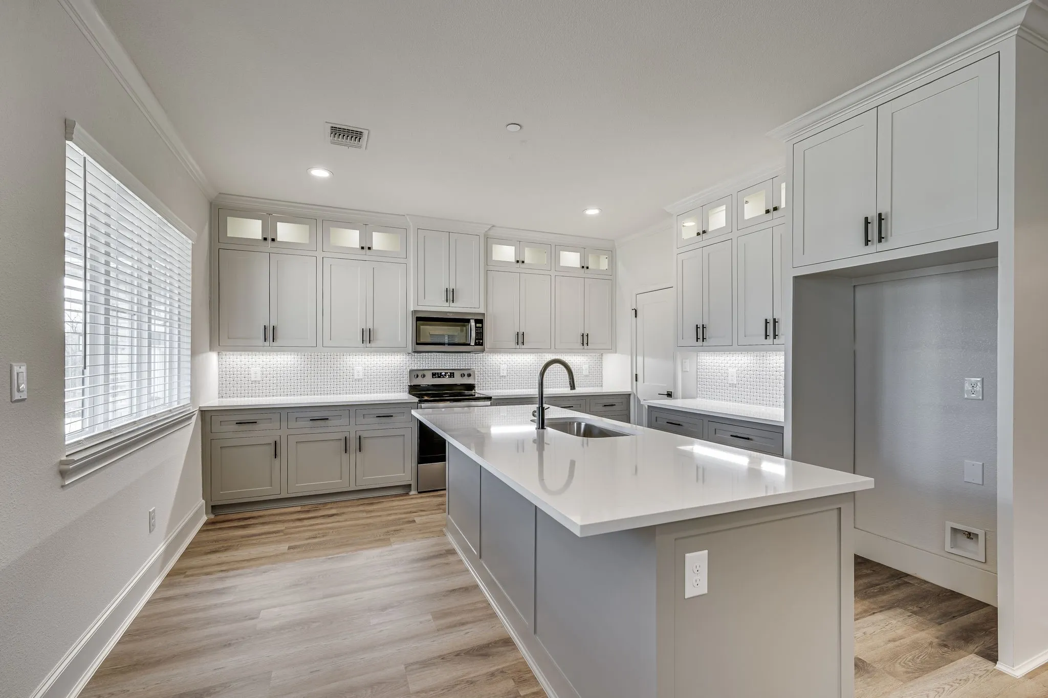 Kitchen with glass insert cabinets, stainless steel appliances, a kitchen island with sink, light wood-style floors, and recessed lighting