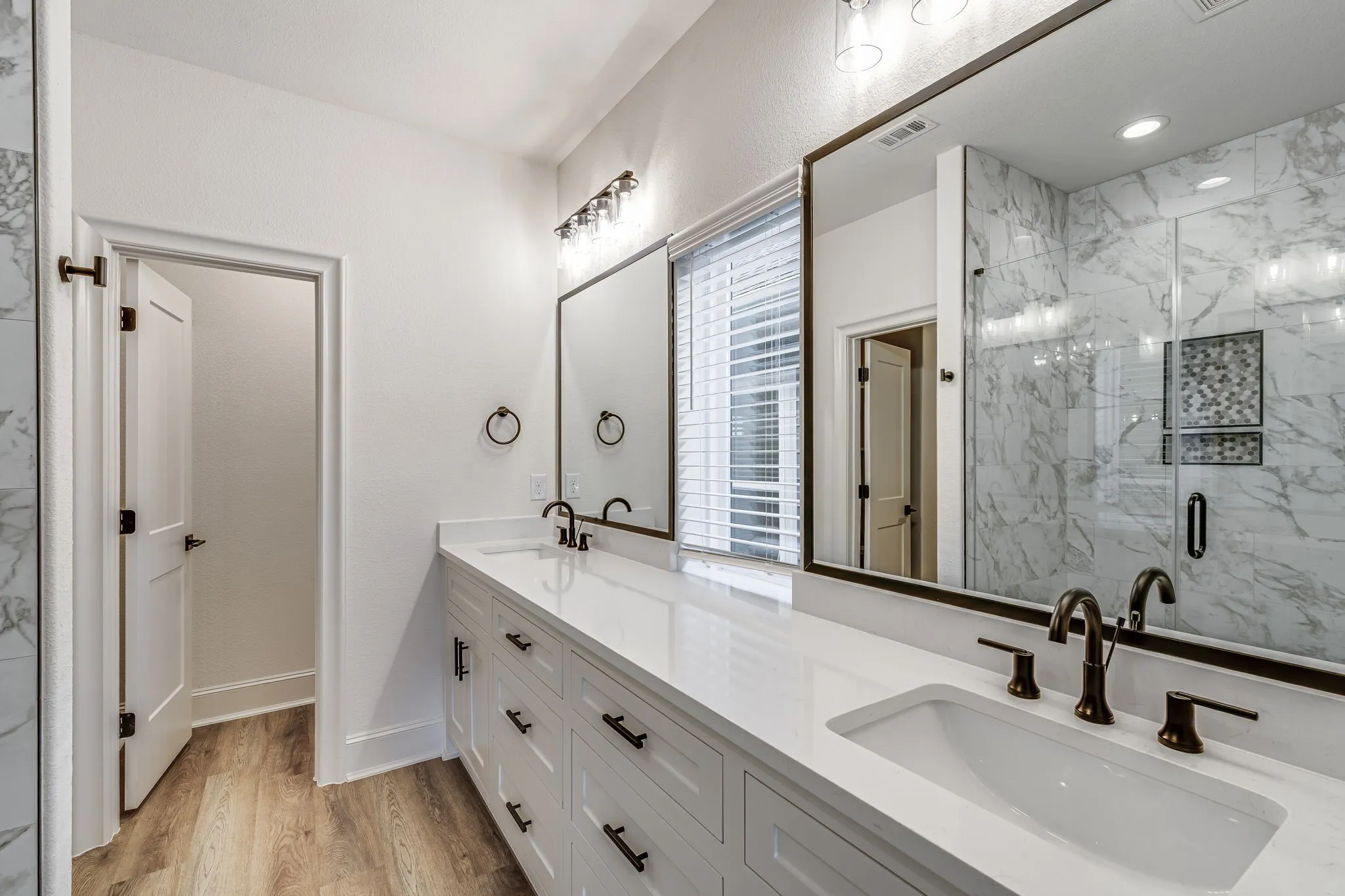 Bathroom featuring double vanity, a marble finish shower, and light wood-style flooring