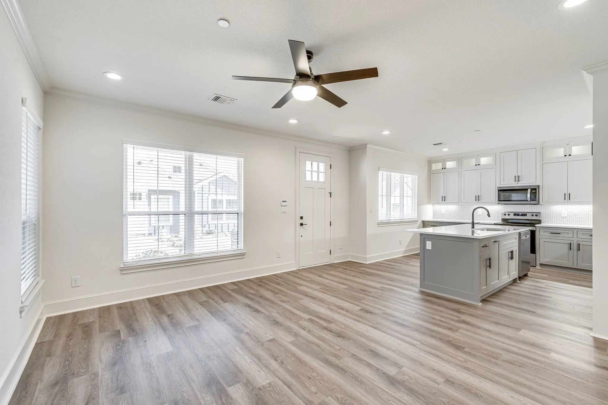 Kitchen featuring crown molding, ceiling fan, glass insert cabinets, open floor plan, and a center island with sink