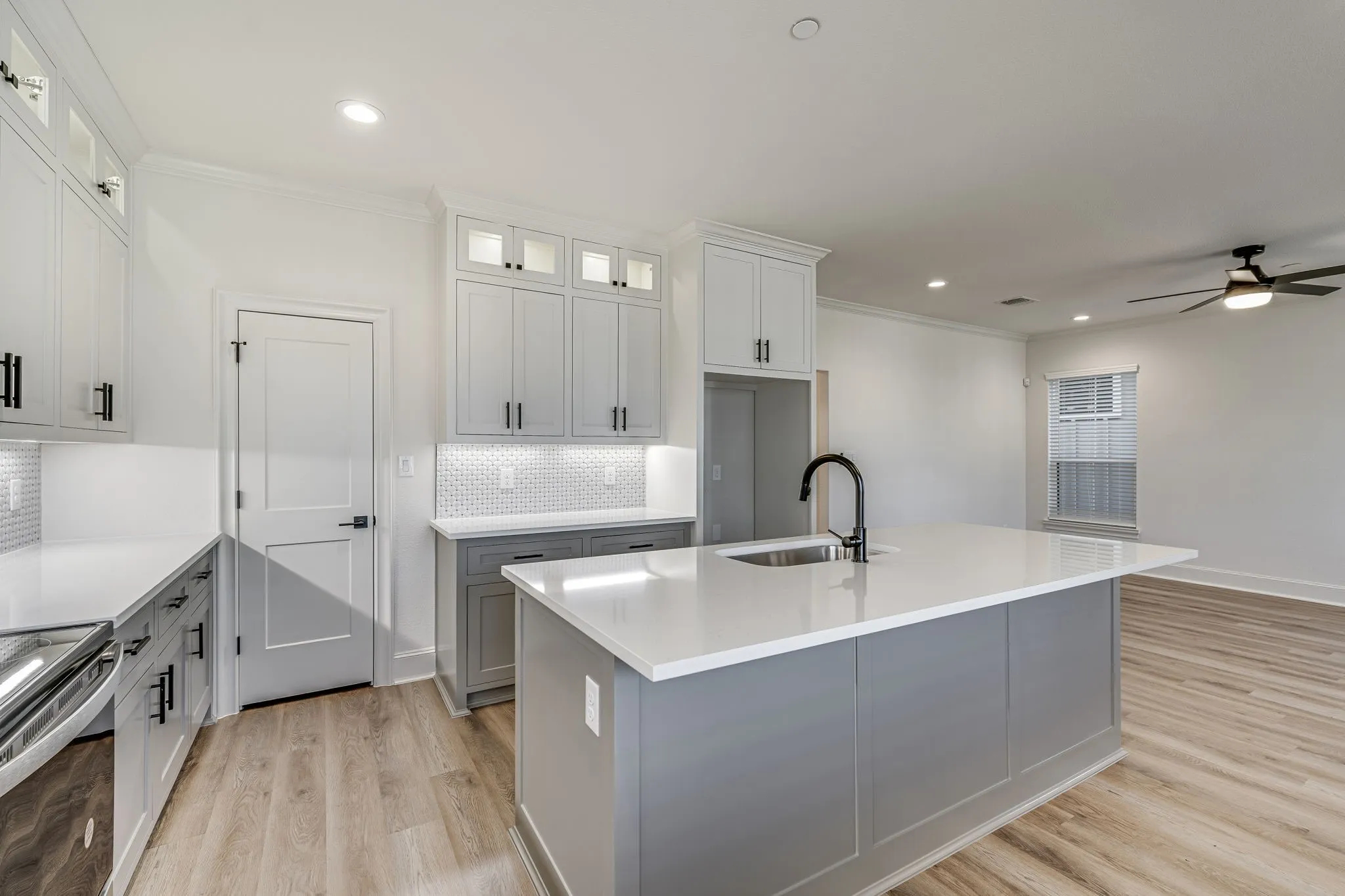 Kitchen featuring glass insert cabinets, tasteful backsplash, an island with sink, dual tone cabinets, and a ceiling fan