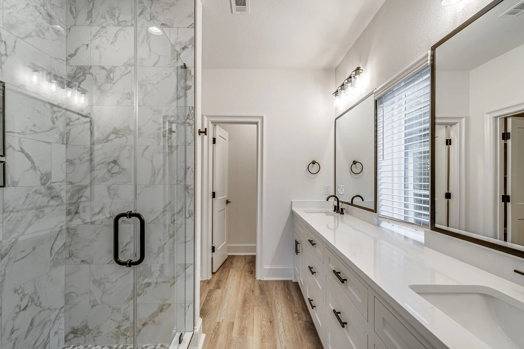 Bathroom featuring double vanity, a marble finish shower, and light wood-style floors