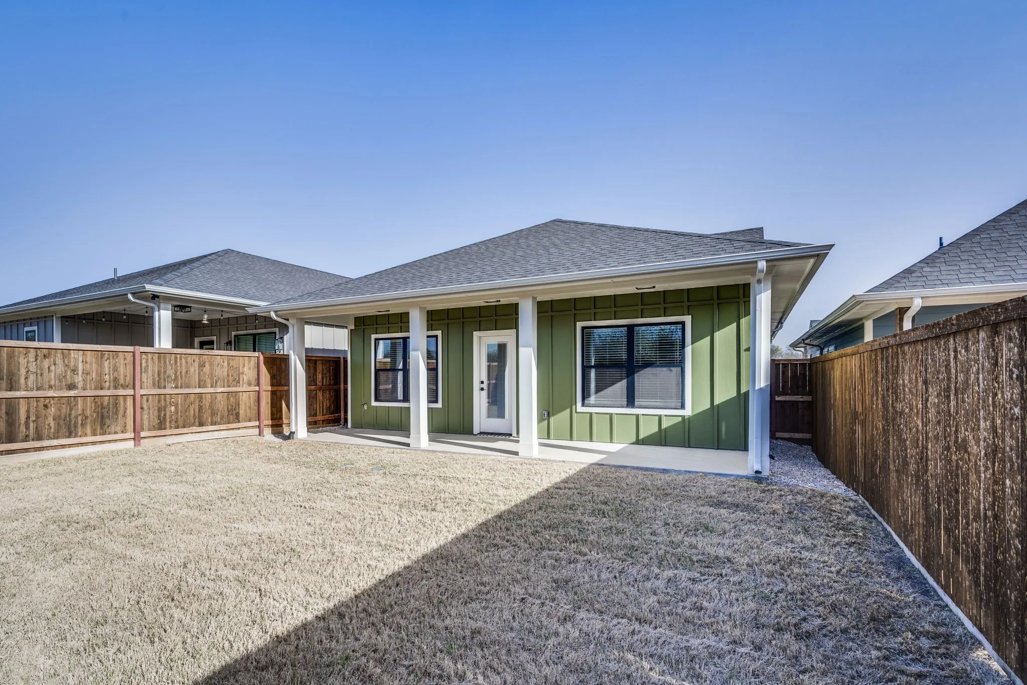 Rear view of property with board and batten siding, a patio area, a shingled roof, and a fenced backyard