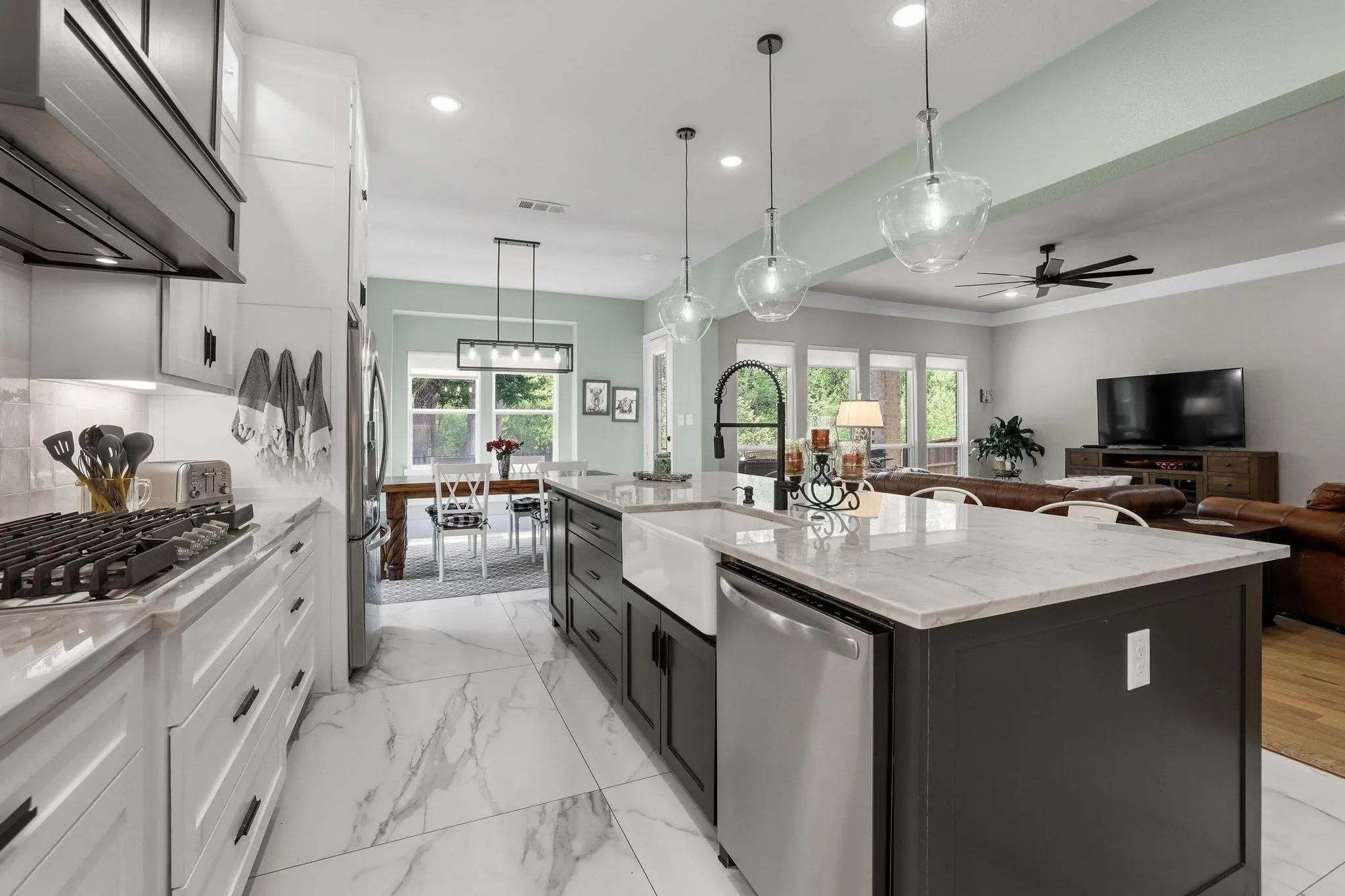 Kitchen with two tone cabinets, light stone countertops, open floor plan, stainless steel appliances, and pendant lighting