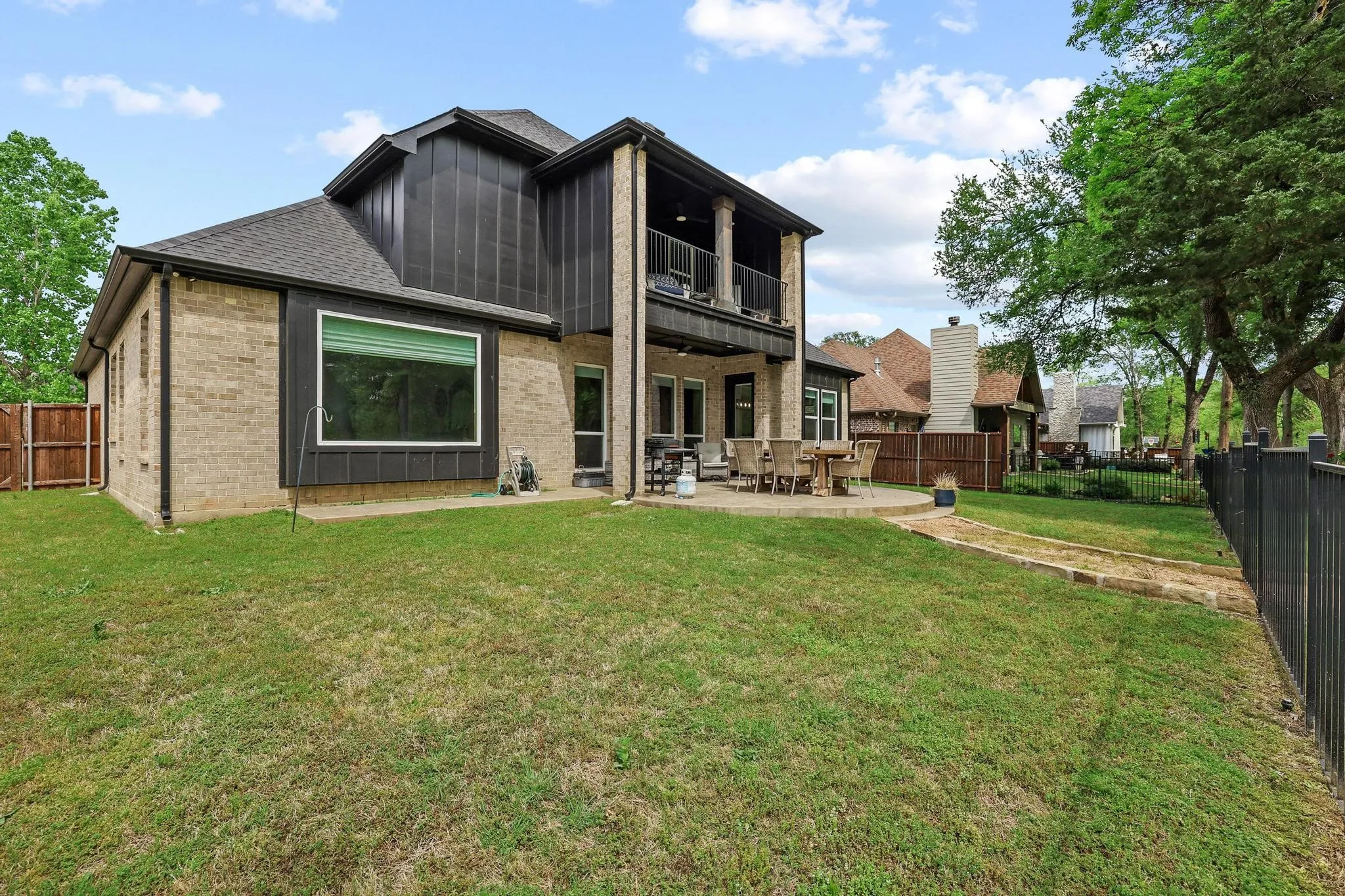 Rear view of property with brick siding, a balcony, a patio area, board and batten siding, and a fenced backyard