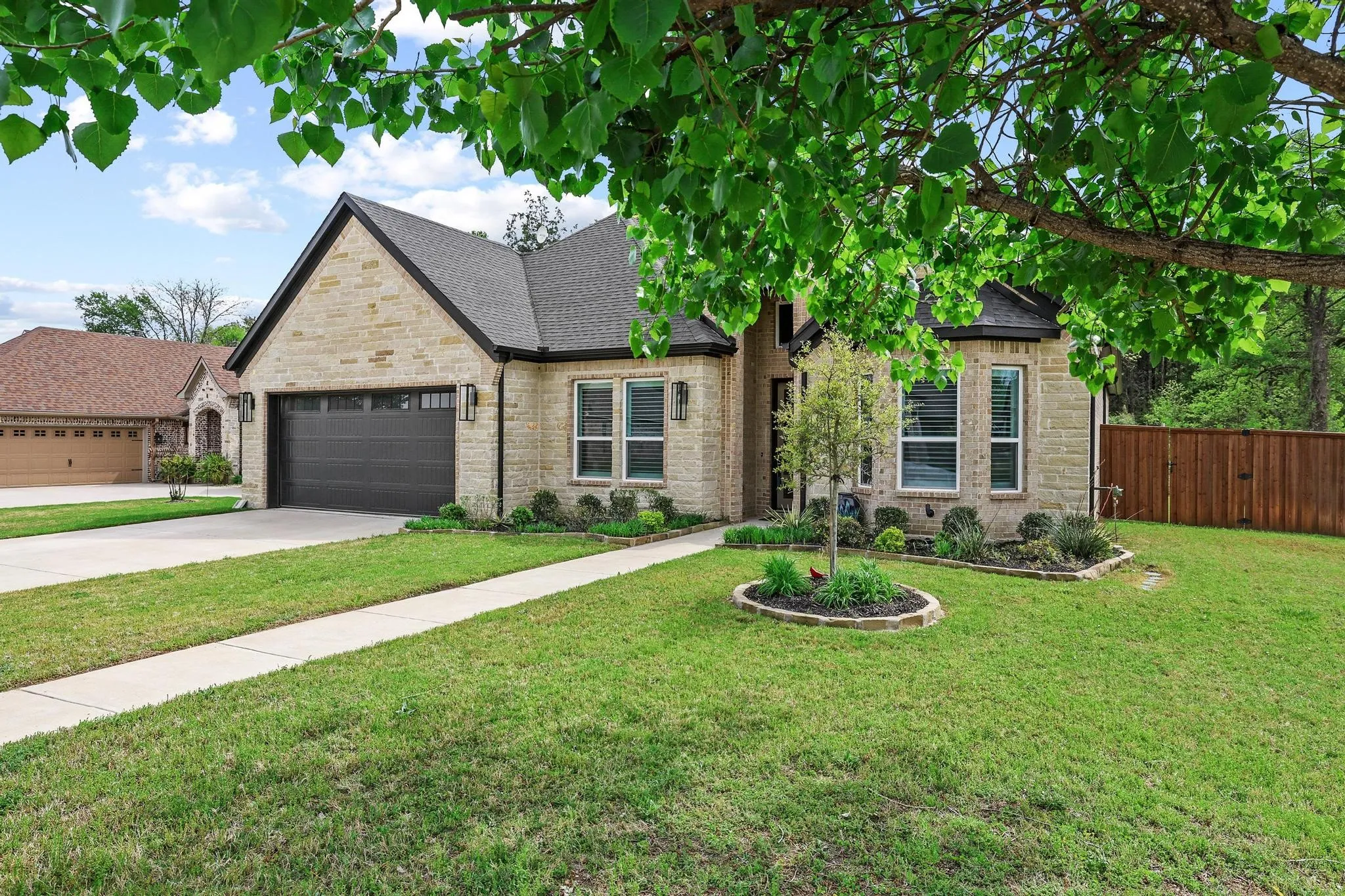 French country inspired facade with driveway, a garage, roof with shingles, and brick siding