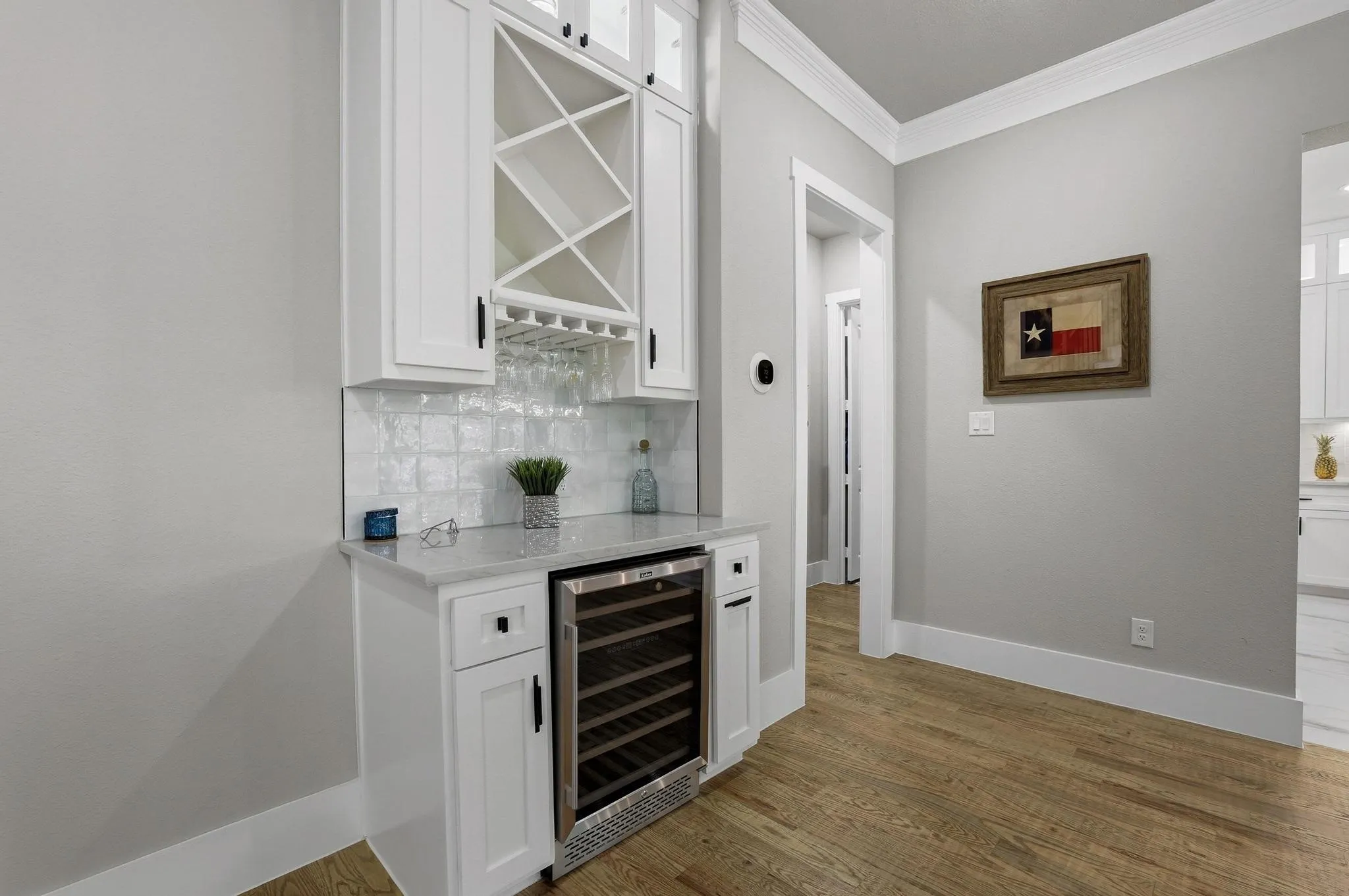 Indoor dry bar with white cabinetry, light stone countertops, wine cooler, ornamental molding, and backsplash