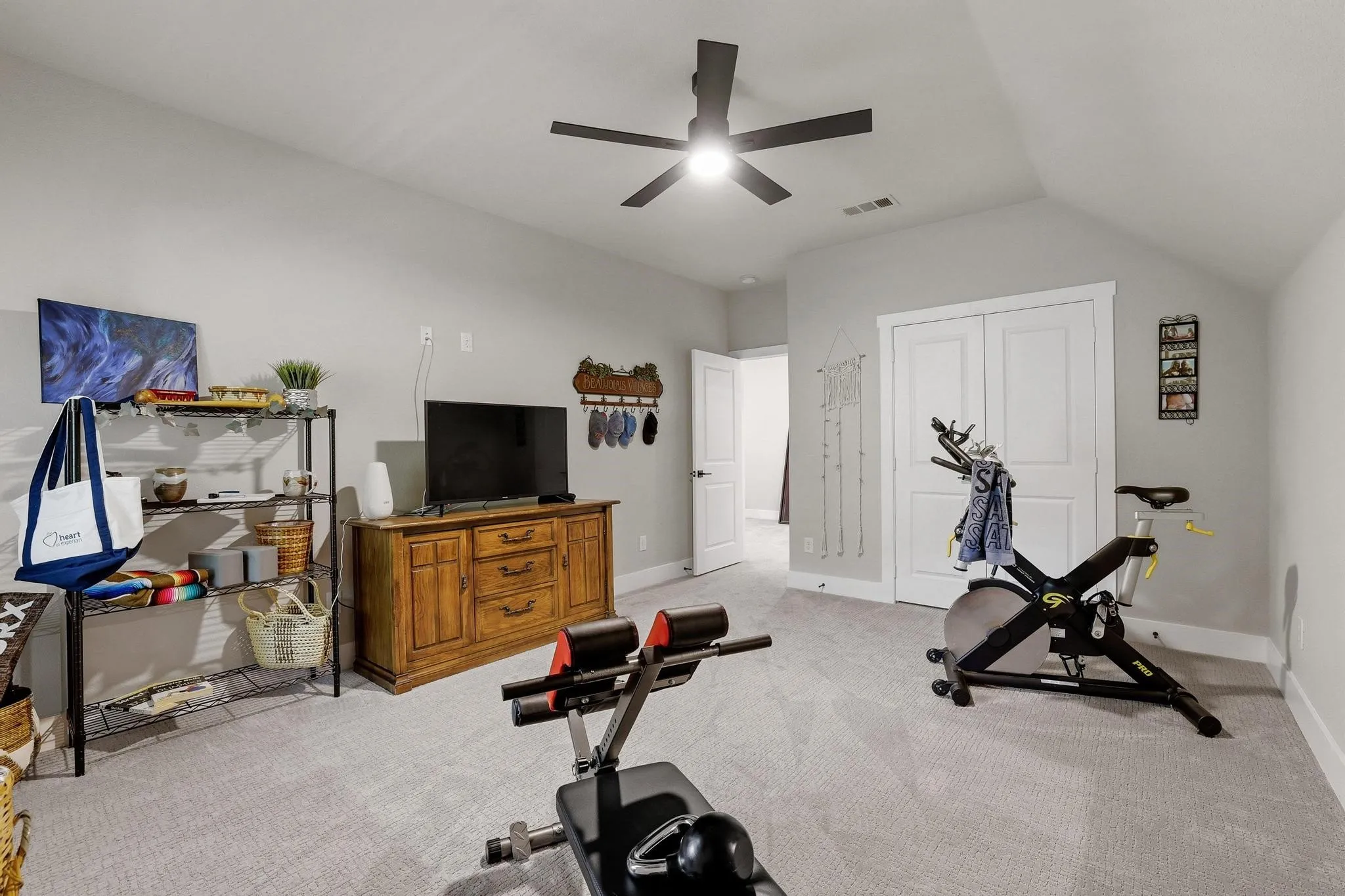 Exercise area with light colored carpet, ceiling fan, and vaulted ceiling