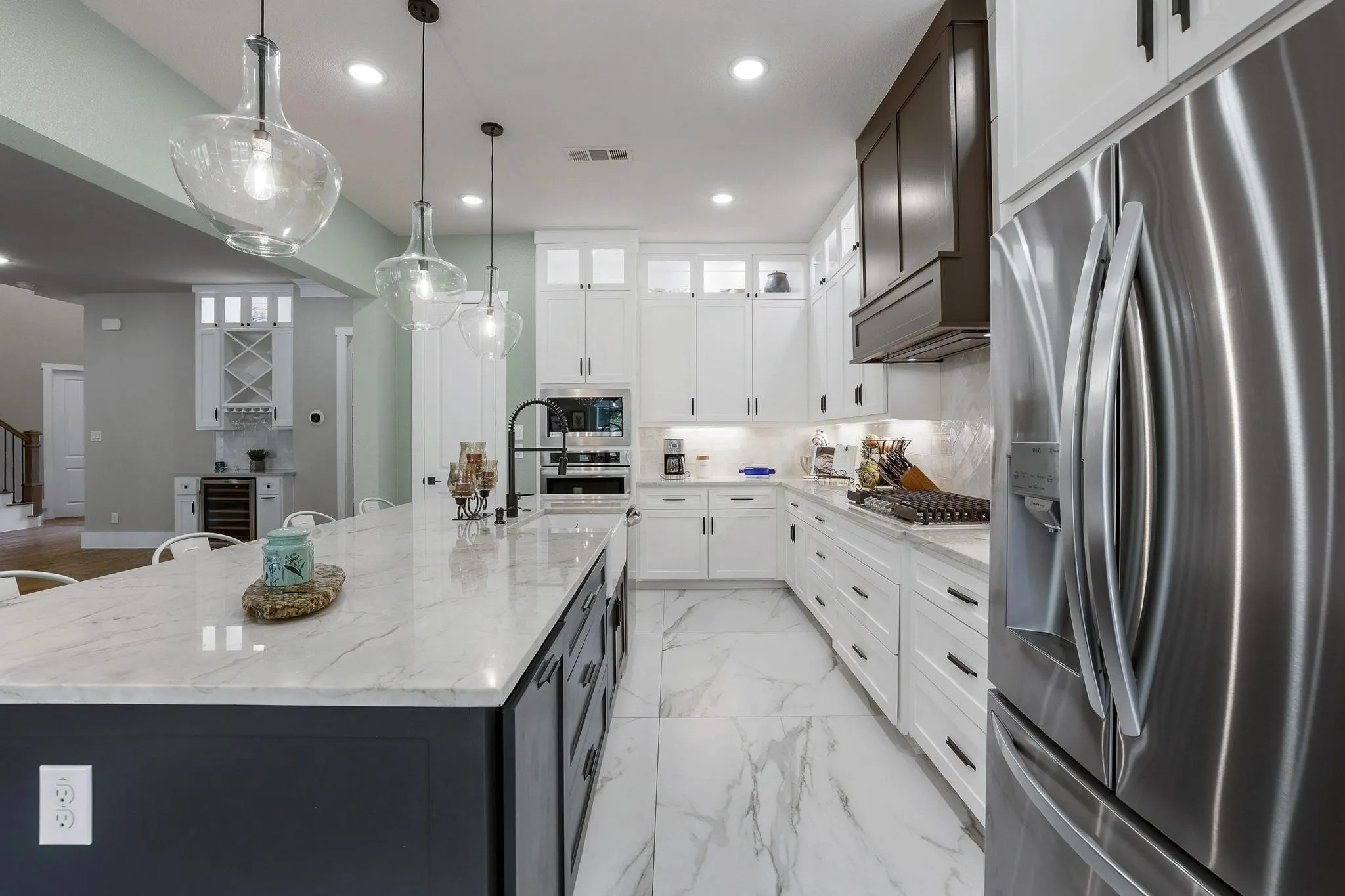 Dual tone kitchen featuring stainless steel appliances, dual tone cabinetry, light stone counters, a large island with sink, and hanging light fixtures
