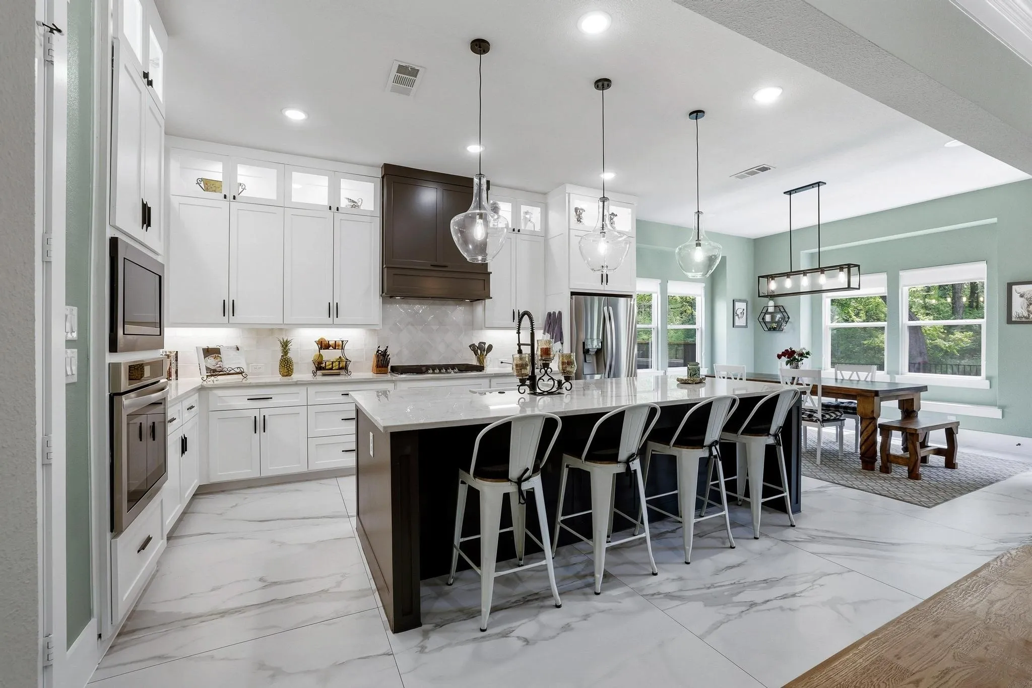 Kitchen featuring a breakfast bar, pendant lighting, a kitchen island with sink, two tone cabinets, and light stone countertops
