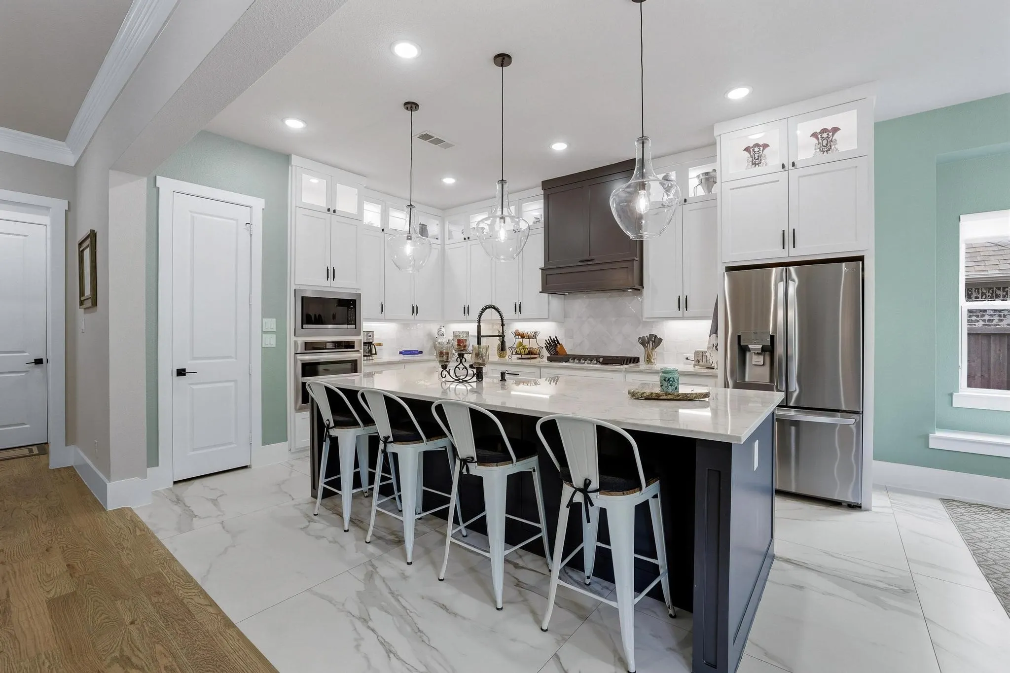 Dual tone kitchen with light marble finish flooring, glass fronted cabinets, stainless steel appliances, decorative light fixtures, and a breakfast bar area