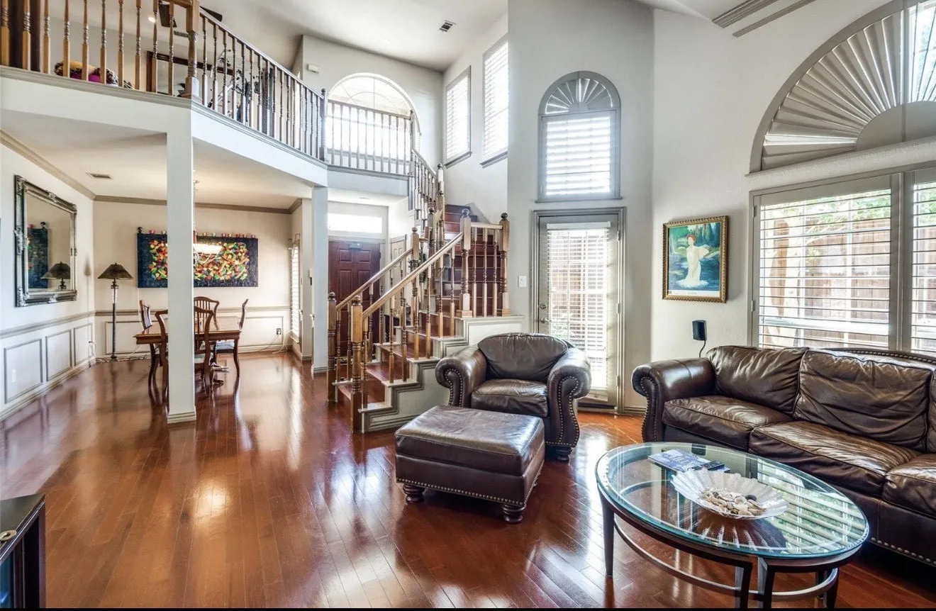 Living room with wood-type flooring, ornamental molding, a high ceiling, a decorative wall, and a wainscoted wall