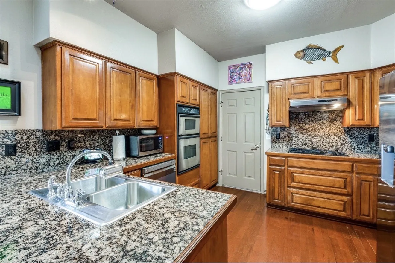 Kitchen featuring wood finish cabinetry, decorative backsplash, dark wood-style flooring, and stainless steel appliances