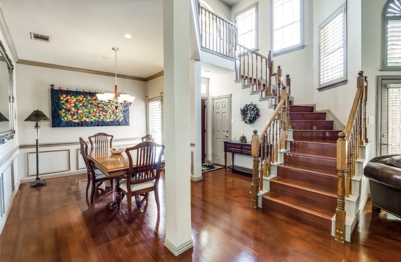 Dining room featuring dark wood-style flooring, a decorative wall, crown molding, hanging lights, and wainscoting
