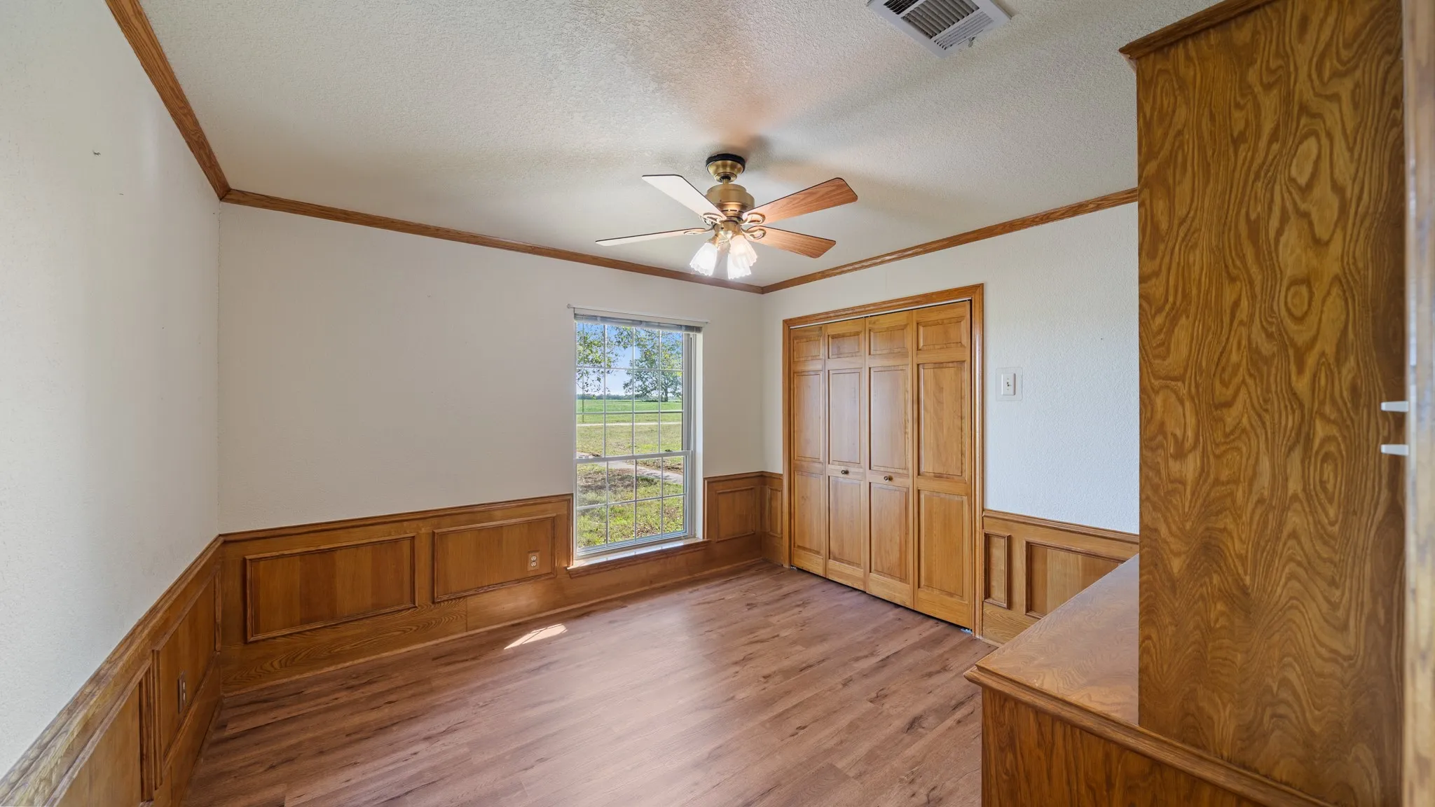 Unfurnished bedroom with ceiling fan, wainscoting, light wood-style flooring, a textured ceiling, and a closet