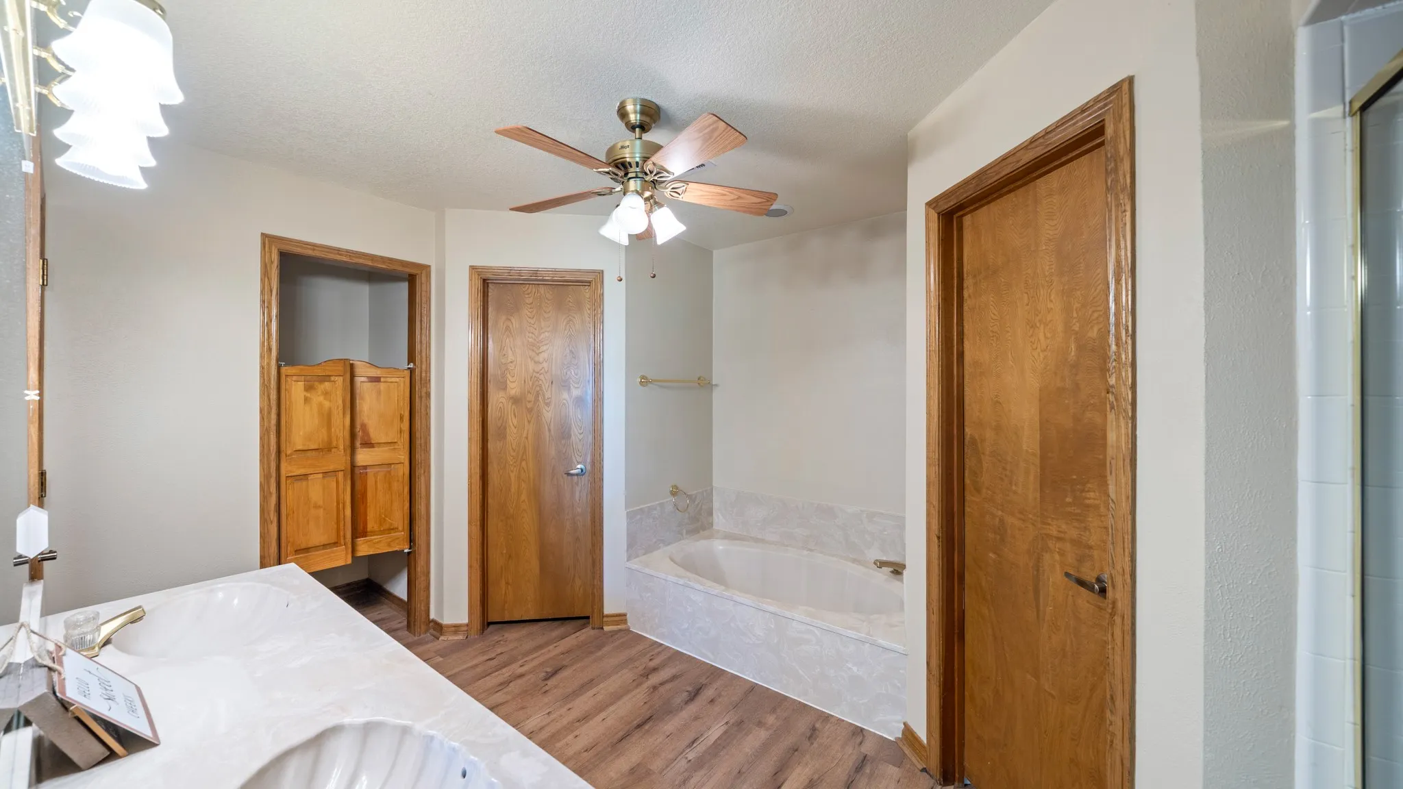 Bathroom with double vanity, a ceiling fan, light wood finished floors, a garden tub, and a textured ceiling