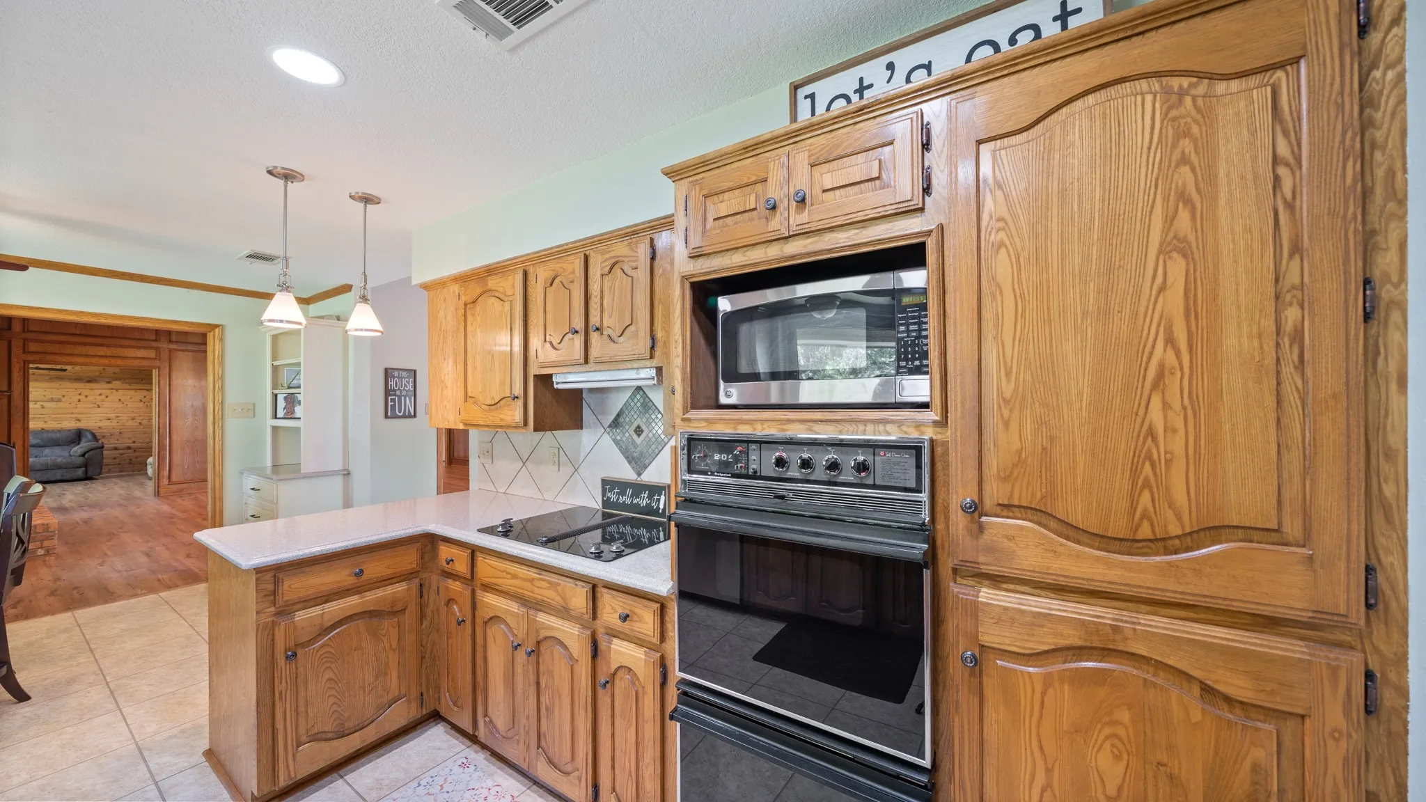 Kitchen with black appliances, a peninsula, pendant lighting, light tile patterned floors, and ornamental molding